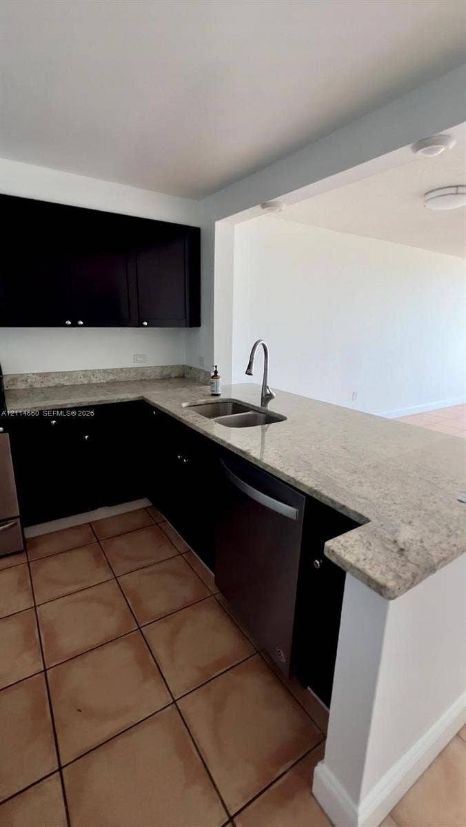 Kitchen featuring dark wood-finish cabinetry, stone countertops, stainless steel dual-basin sink, high-arch faucet, and tile flooring