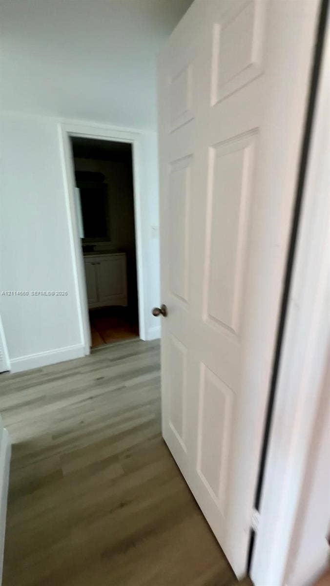 Six-panel interior door with a satin-nickel lever handle, wood-finish flooring, and white interior trim