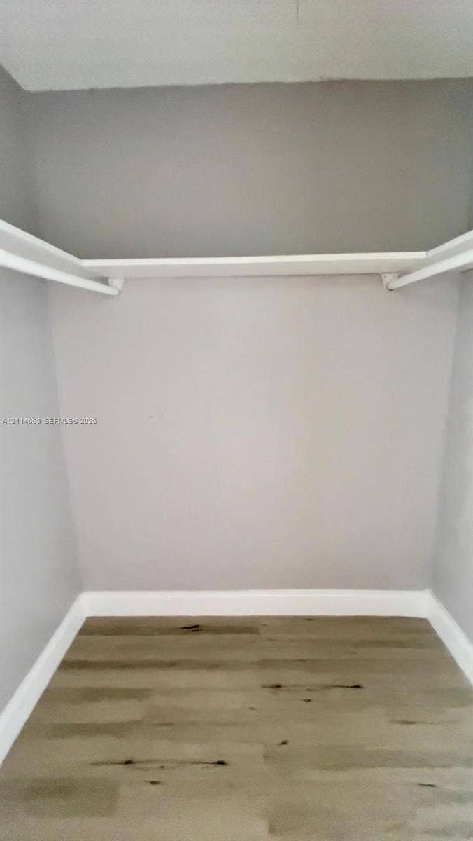 Walk-in closet featuring wood-finish flooring and built-in shelving with integrated rods