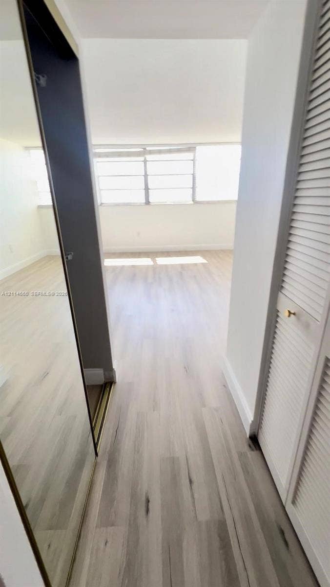 Interior space featuring light-toned wood-finish flooring, floor-to-ceiling mirrored closet doors, and louvered closet cabinetry with metallic hardware