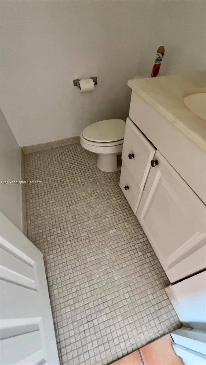 Bathroom featuring a vanity with an integrated basin, white cabinetry, mosaic tile flooring, and a wall-mounted paper holder