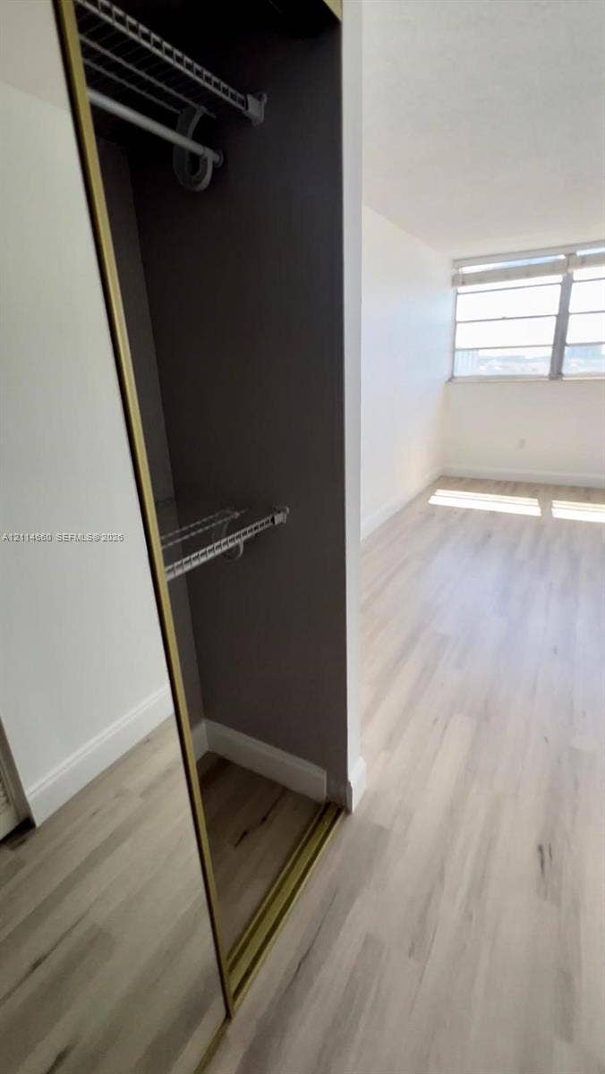 Closet with sliding mirrored doors, interior wire shelving, wood-finish flooring, and horizontal window blinds