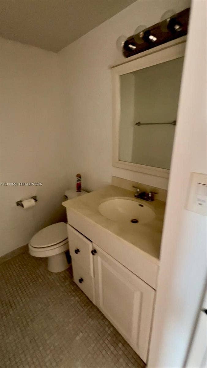 White vanity cabinet with an integrated sink, neutral countertop, rectangular framed mirror, and multi-bulb vanity lighting
