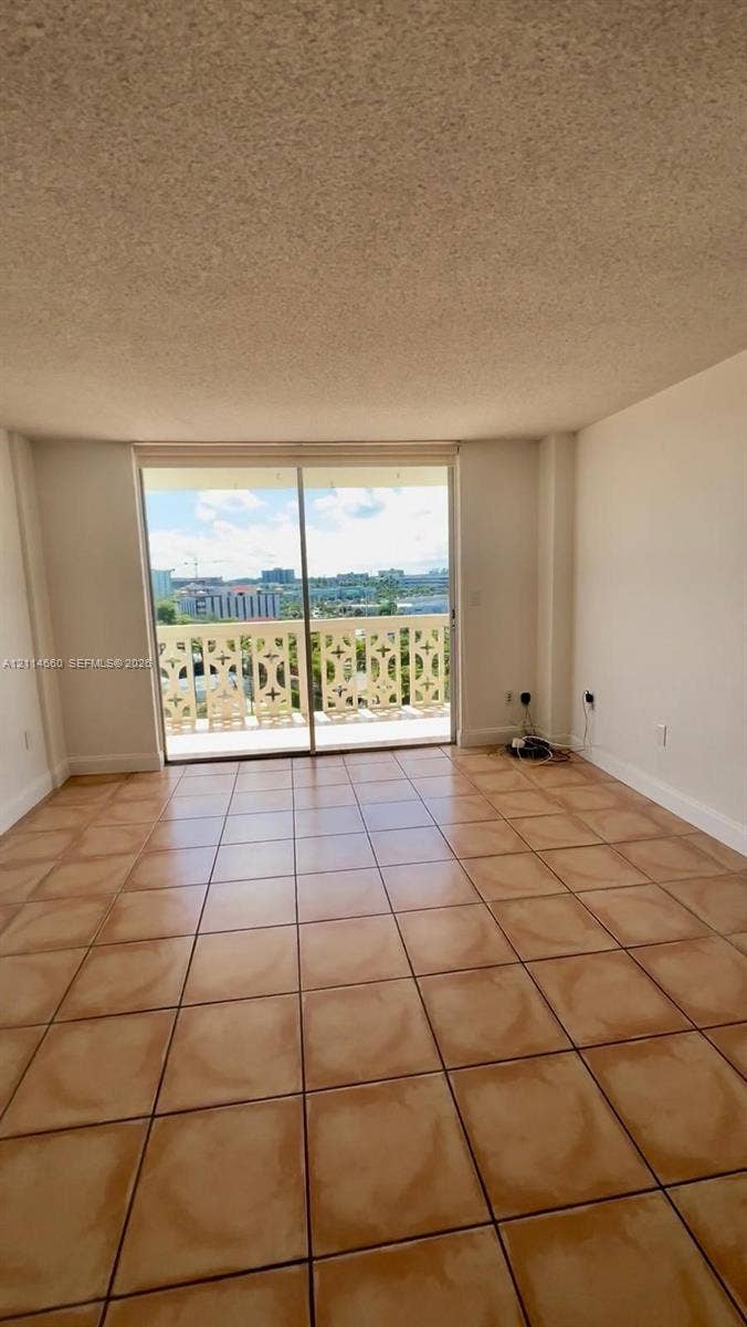 Interior space featuring ceramic tile flooring, textured ceiling, and sliding glass door access to a balcony with decorative railing
