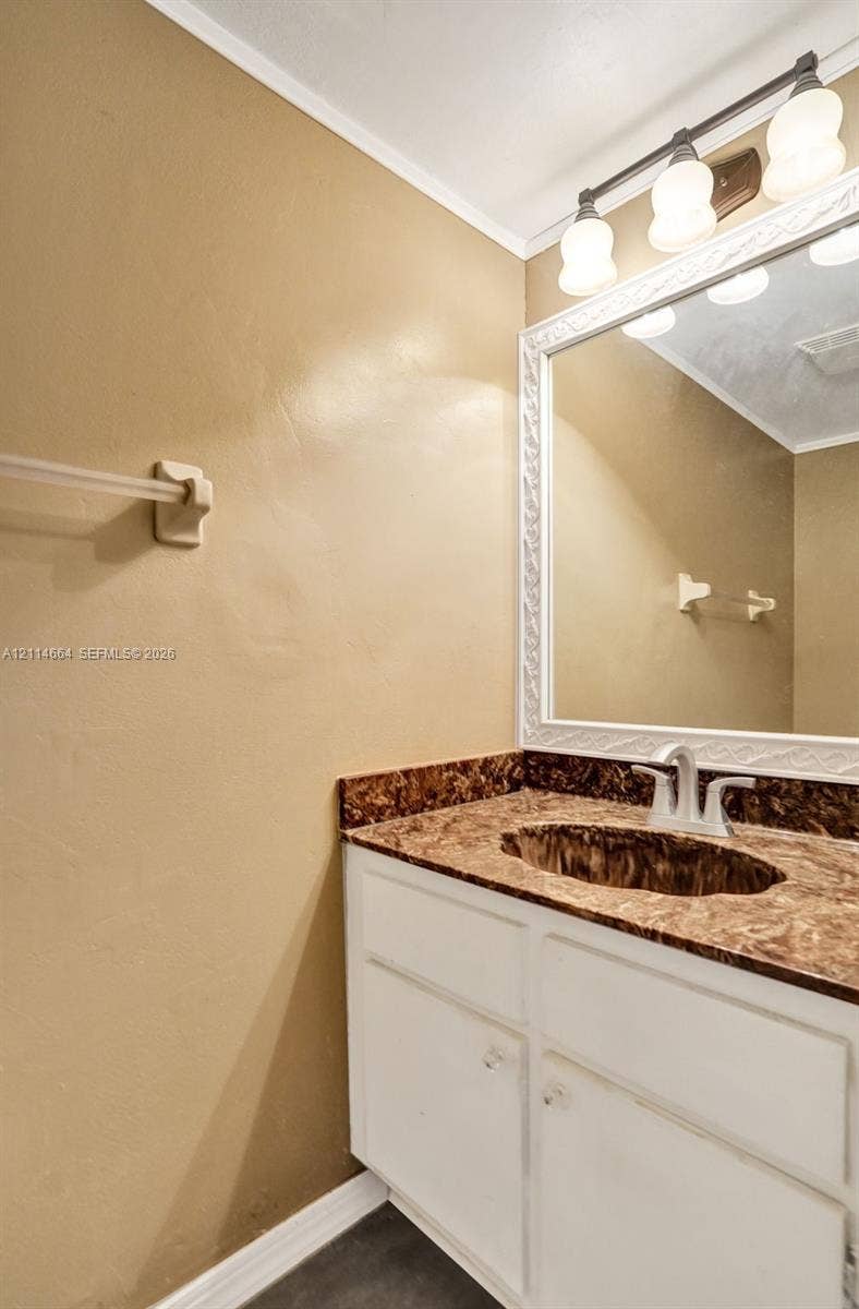 11164 NW 10th Place, Coral Springs, FL 33071 Vanity featuring a white cabinet, integrated sink, stone-finish countertop, decorative framed mirror, and three-bulb vanity light fixture
