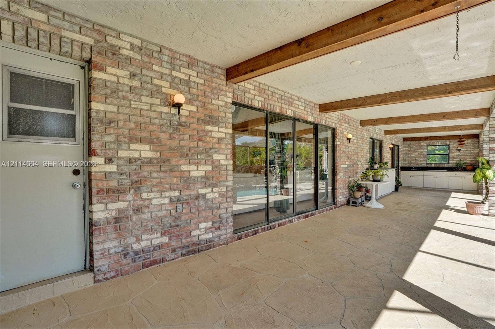 11164 NW 10th Place, Coral Springs, FL 33071 Covered patio featuring exposed wood ceiling beams, multi-tonal brick masonry, flagstone-style flooring, sliding glass doors, and built-in cabinetry