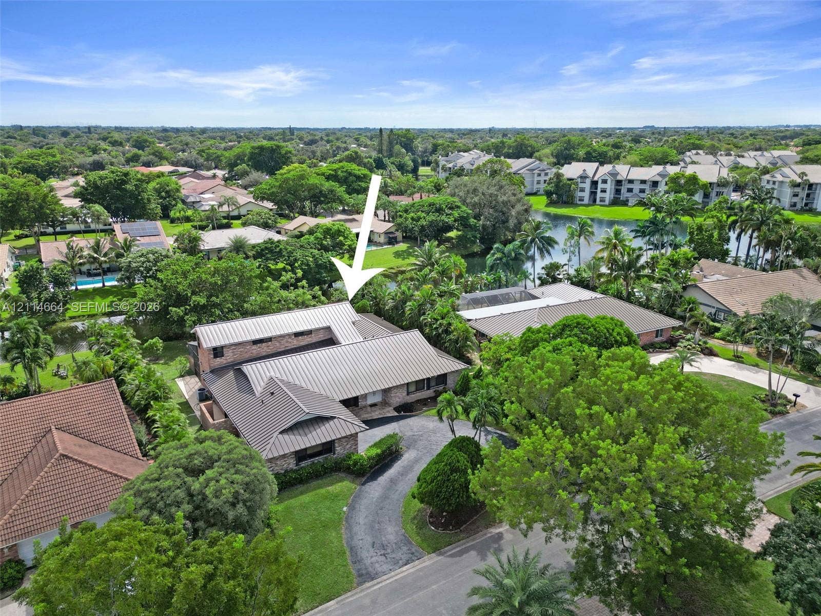 11164 NW 10th Place, Coral Springs, FL 33071 Aerial view featuring a multi-pitched metal roof, brick exterior cladding, curved driveway, and lush perimeter landscaping situated along a waterway