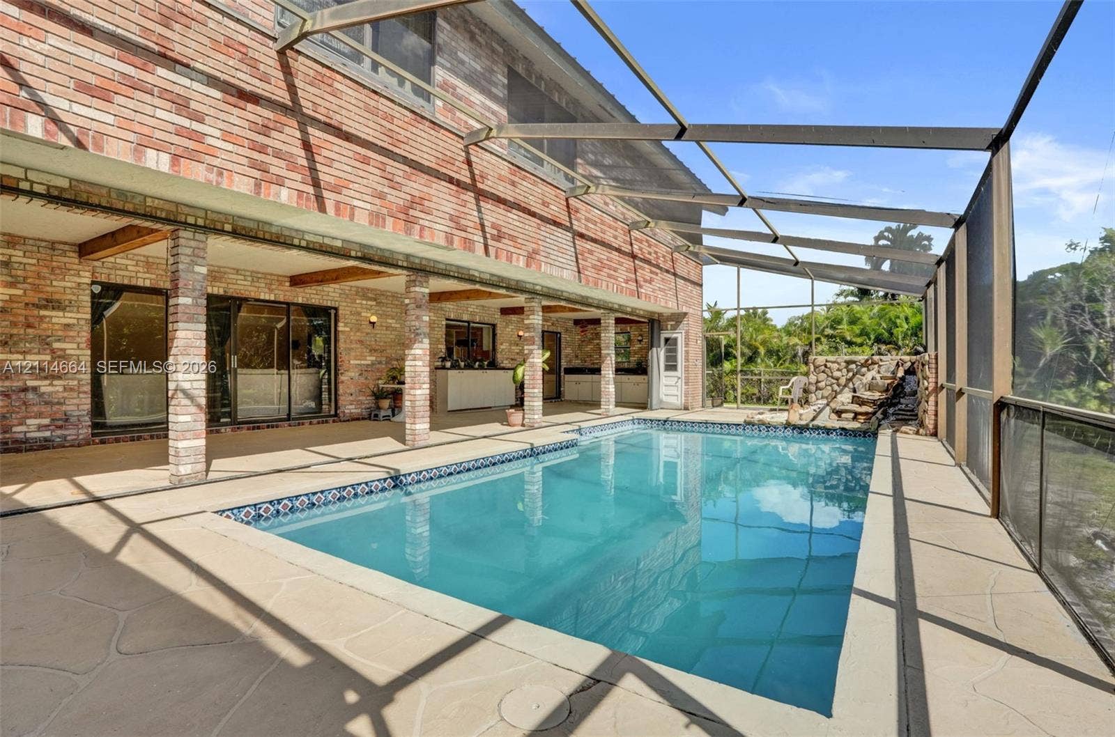 11164 NW 10th Place, Coral Springs, FL 33071 Screened lanai featuring a swimming pool, stone-accented water feature, brick exterior wall, and covered patio space