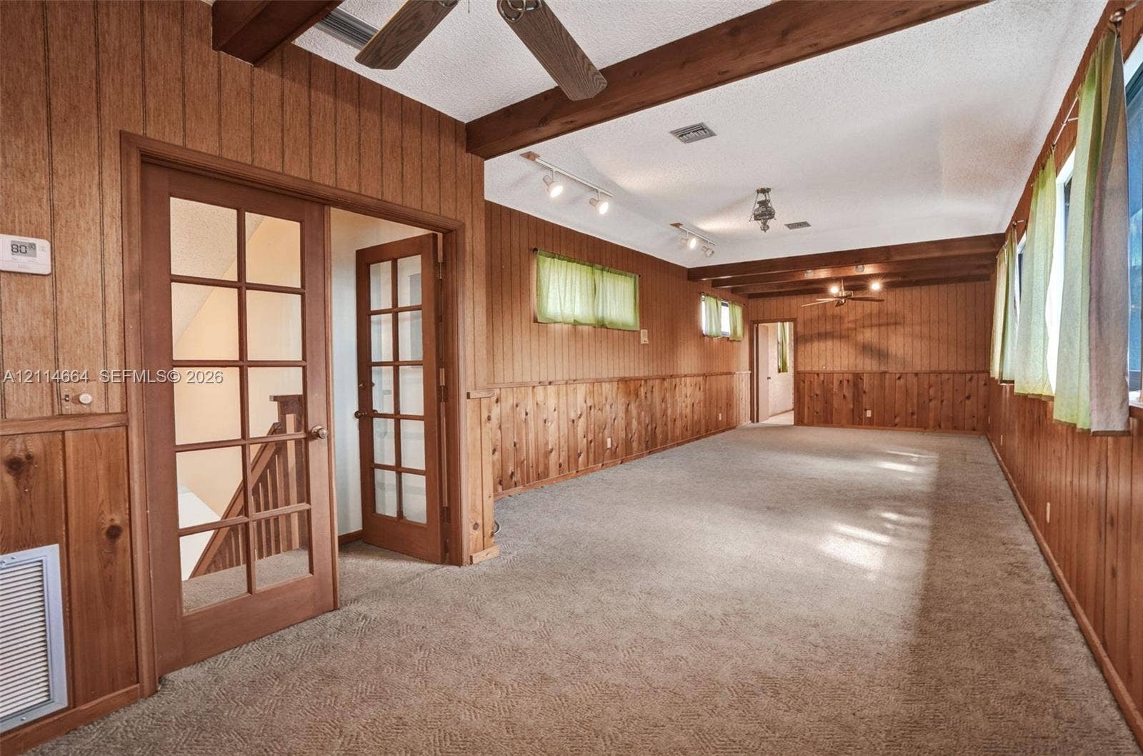 11164 NW 10th Place, Coral Springs, FL 33071 Wood-paneled interior featuring exposed structural ceiling beams, French doors with glass panes, wall-mounted track lighting, and ceiling fans