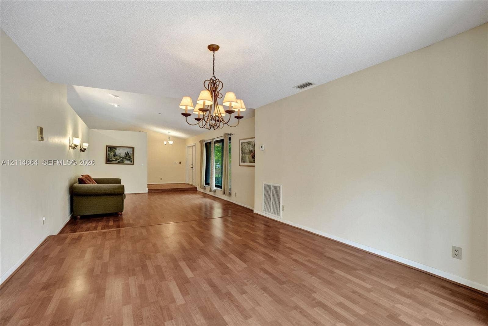 11164 NW 10th Place, Coral Springs, FL 33071 Open interior featuring wood-finish flooring, a multi-arm metal chandelier, wall-mounted light fixtures, and windows with neutral framing