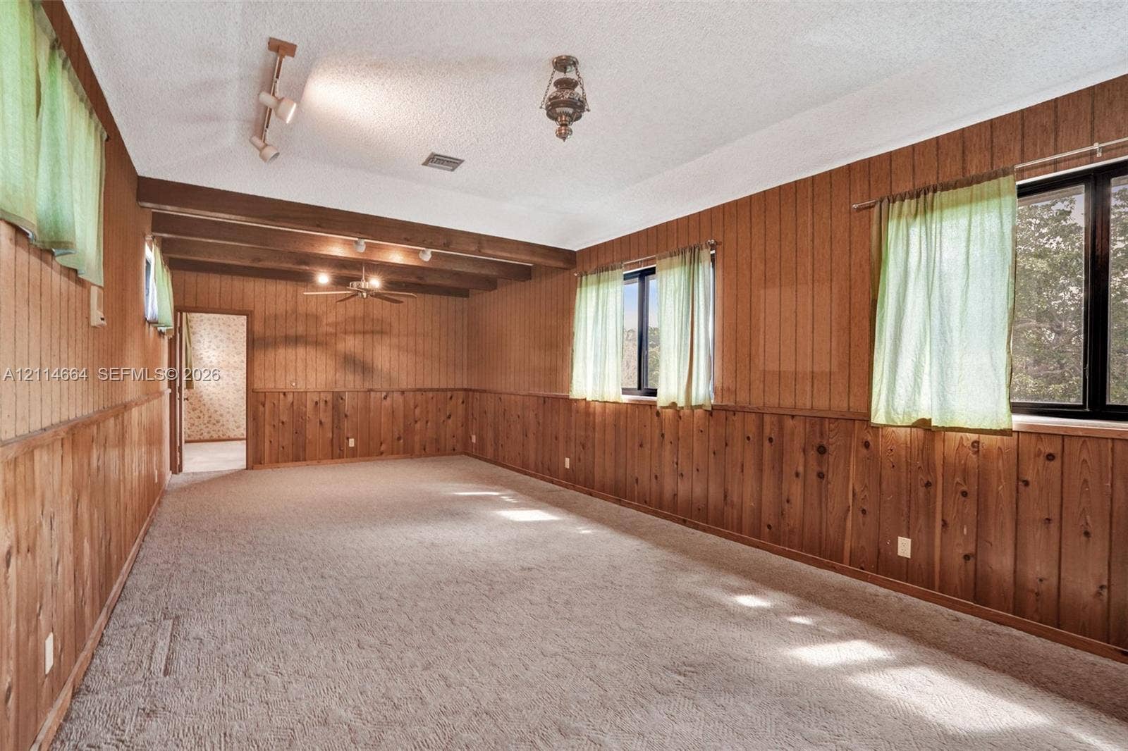 11164 NW 10th Place, Coral Springs, FL 33071 Interior space featuring wood paneling, vaulted ceiling with exposed beams, recessed track lighting, and carpeted flooring
