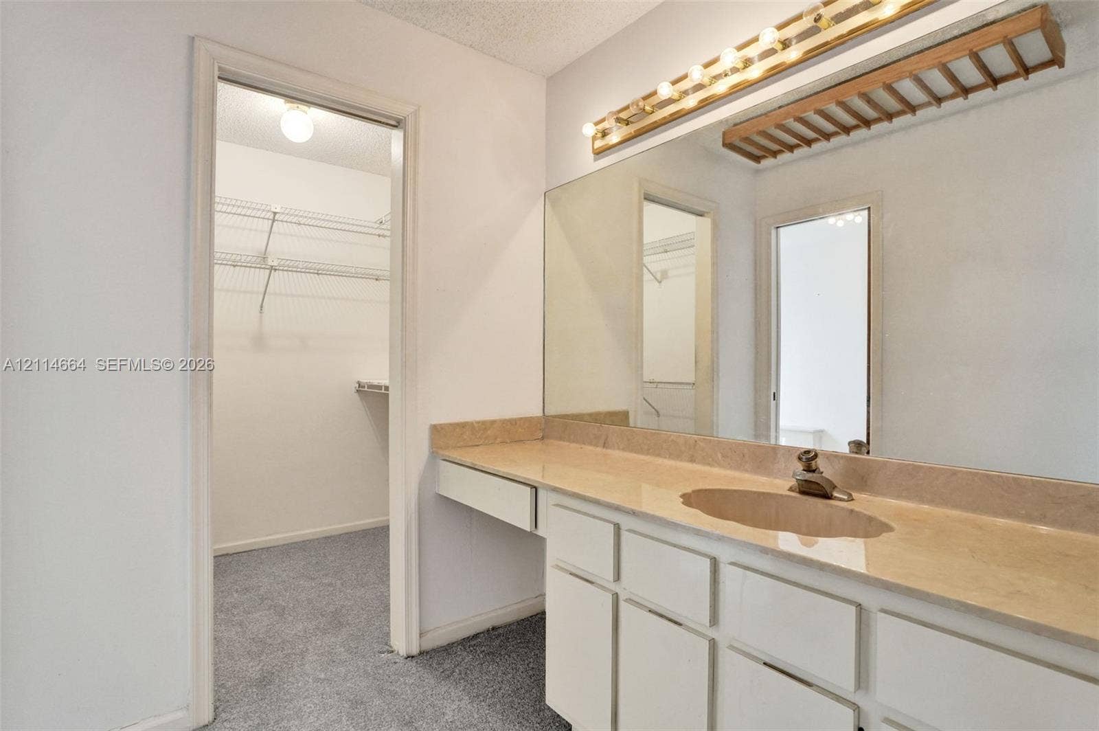 11164 NW 10th Place, Coral Springs, FL 33071 Vanity with neutral-toned solid surface countertop, integrated sink, and full-width mirror with mounted lighting, plus walk-in storage area featuring wire shelving