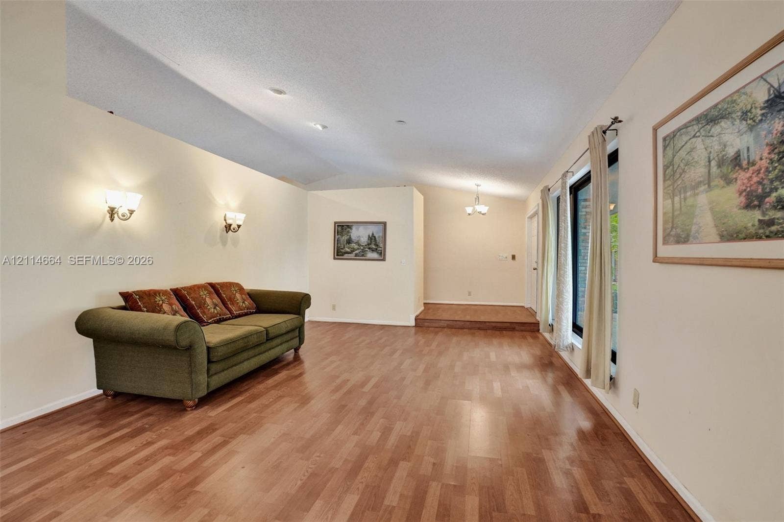11164 NW 10th Place, Coral Springs, FL 33071 Living space featuring vaulted ceilings, wood-finish flooring, wall-mounted light fixtures, and a raised platform area