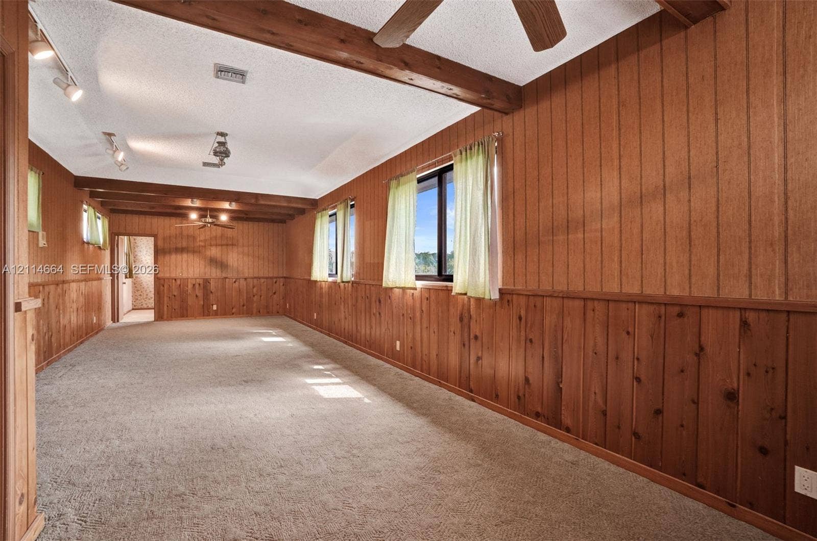 11164 NW 10th Place, Coral Springs, FL 33071 Wood-paneled walls, exposed timber ceiling beams, carpeted flooring, track lighting, and ceiling-mounted fans