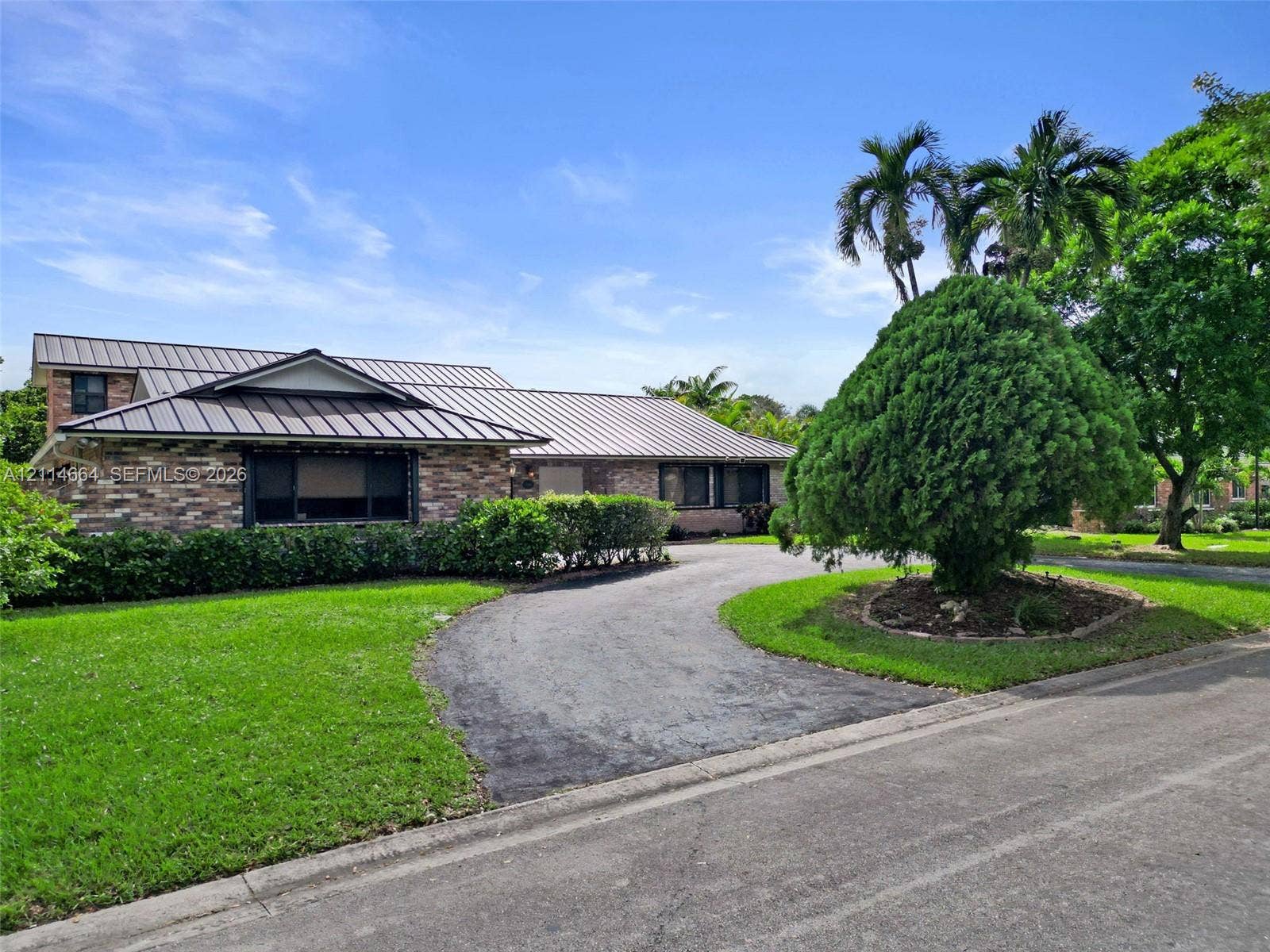 11164 NW 10th Place, Coral Springs, FL 33071 Single-story exterior featuring a brick facade, metal roofing, a curved paved driveway, and established landscaping