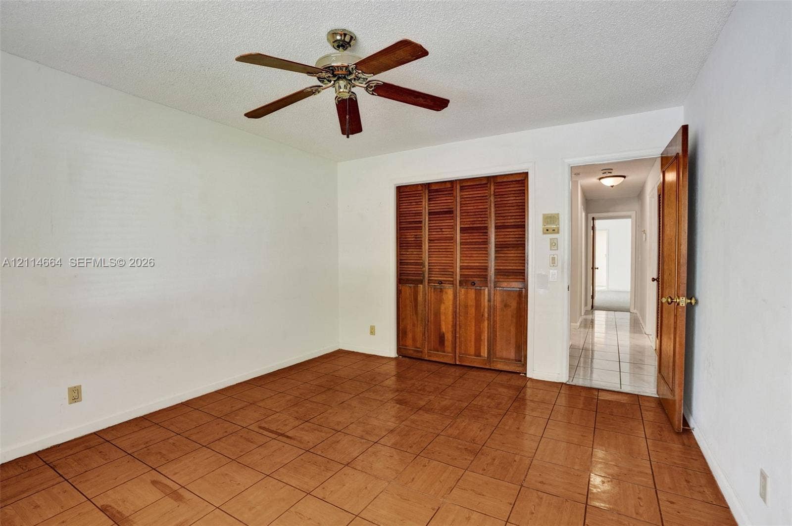 11164 NW 10th Place, Coral Springs, FL 33071 Room featuring square ceramic tile flooring, built-in wooden louvered closet doors, and a ceiling fan with integrated lighting