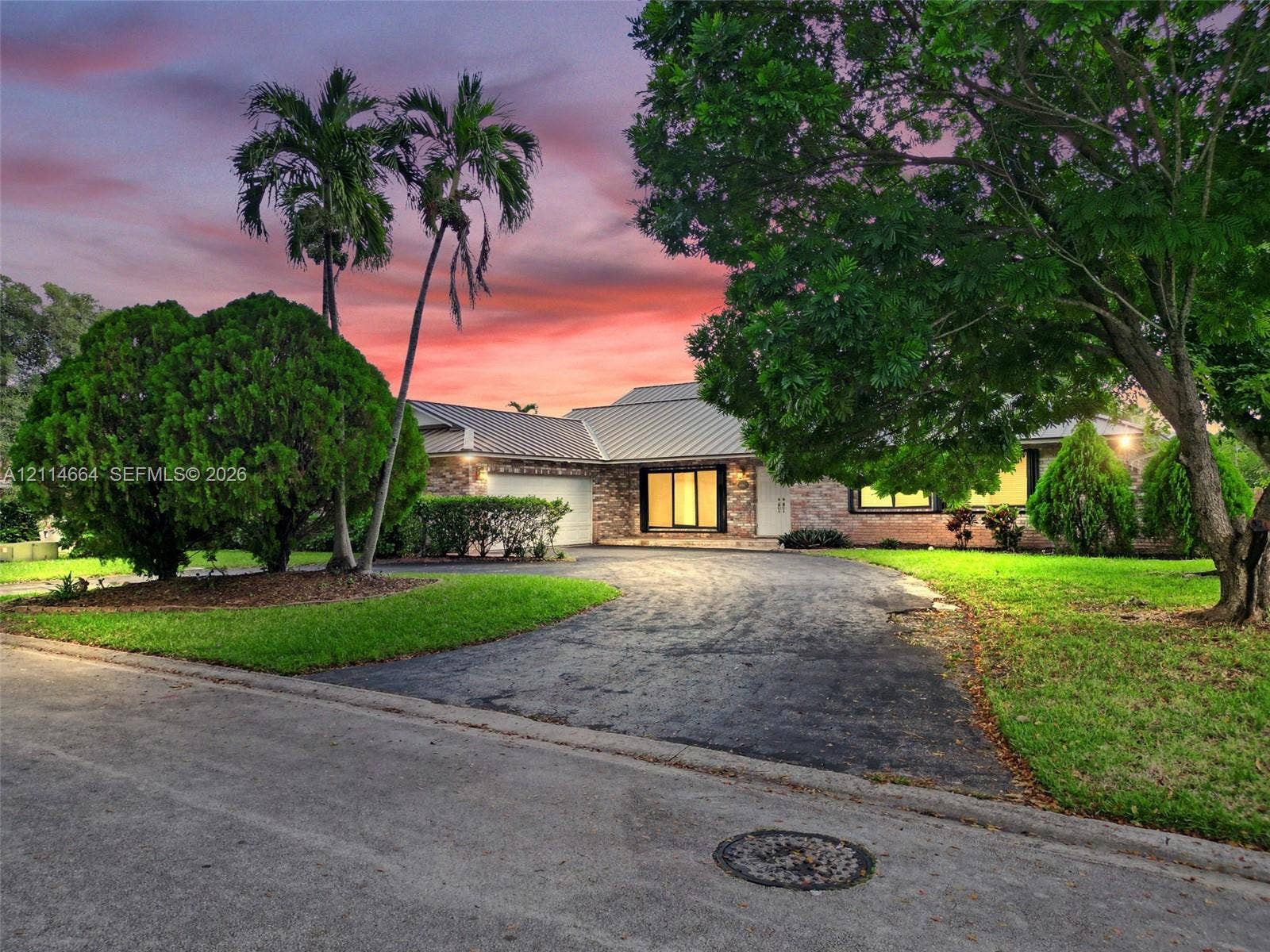 11164 NW 10th Place, Coral Springs, FL 33071 Single-story residence featuring a brick facade, metal roofing, paved driveway, and mature landscaping