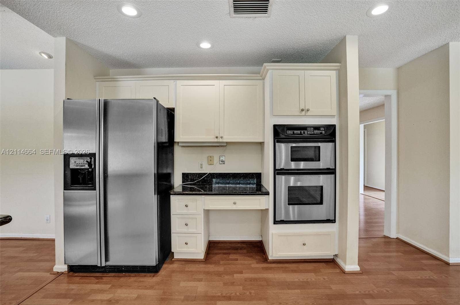 11164 NW 10th Place, Coral Springs, FL 33071 Kitchen featuring off-white cabinetry, dark stone countertops, stainless steel double wall ovens, side-by-side refrigerator, and wood-finish flooring