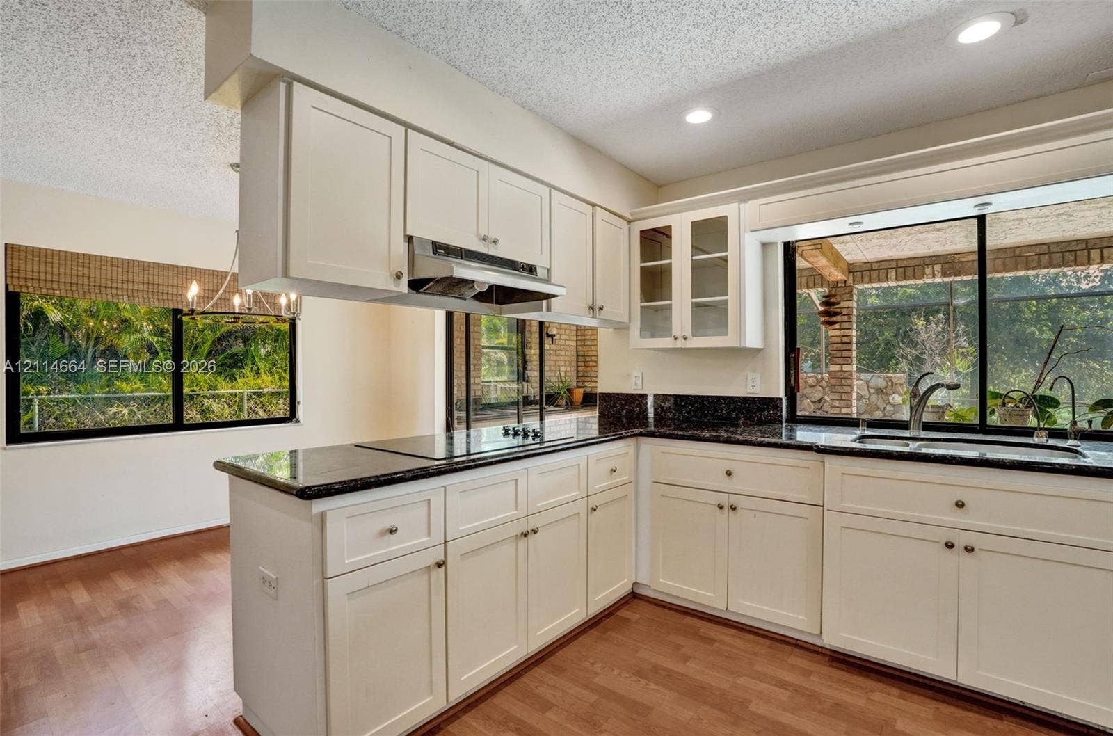 11164 NW 10th Place, Coral Springs, FL 33071 Kitchen featuring white cabinetry, dark stone-finish countertops, glass-panel upper cabinet doors, recessed lighting, and wood-finish flooring