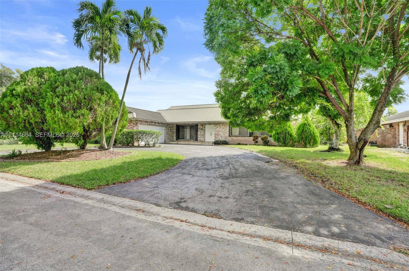 11164 NW 10th Place, Coral Springs, FL 33071 Single-story residence featuring a multi-gabled roofline, light-toned masonry facade, integrated two-car garage, asphalt driveway, and mature landscaping