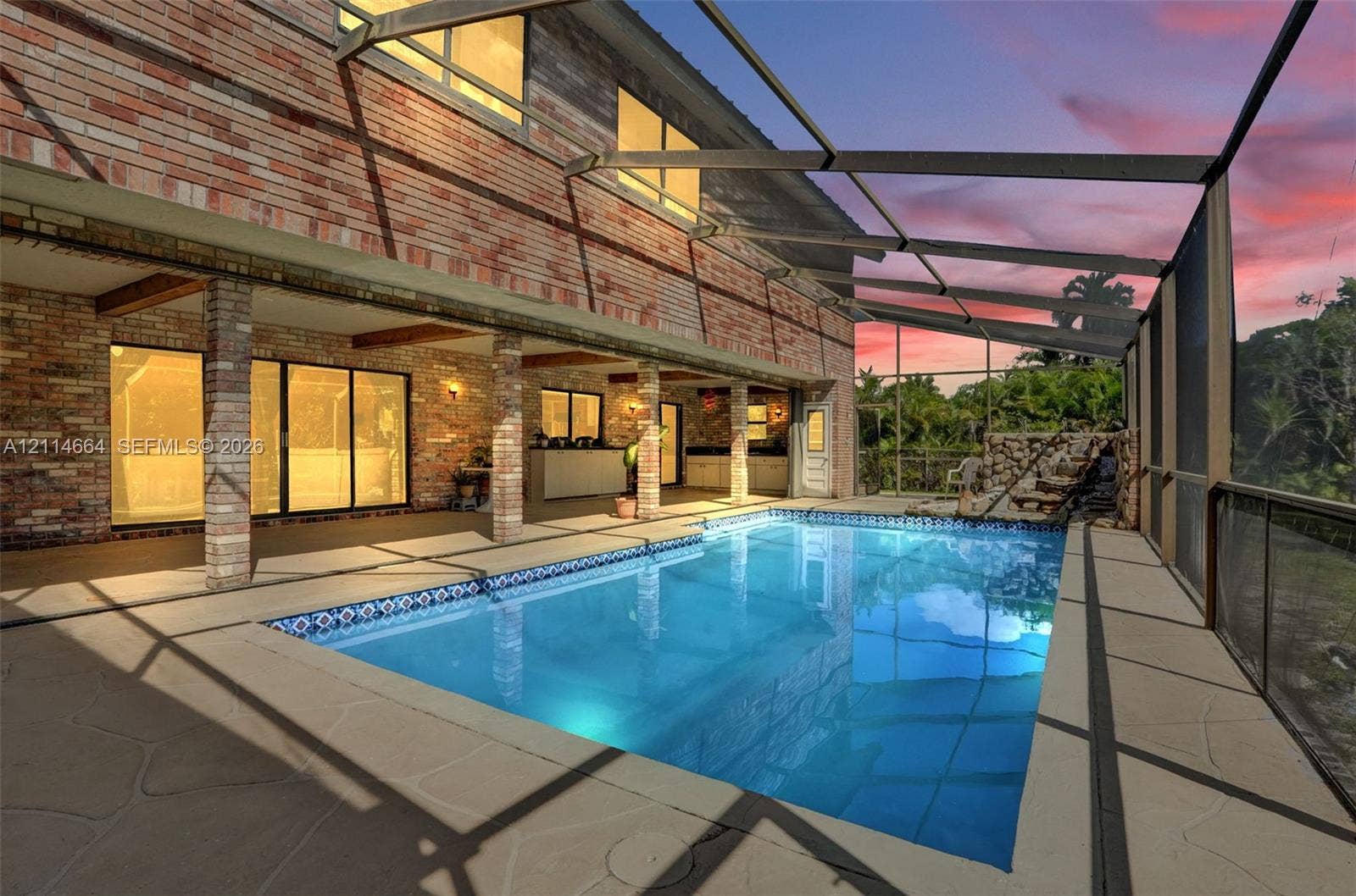 11164 NW 10th Place, Coral Springs, FL 33071 Screened pool enclosure featuring a brick facade, covered patio, rock-style water feature, and exterior masonry pillars