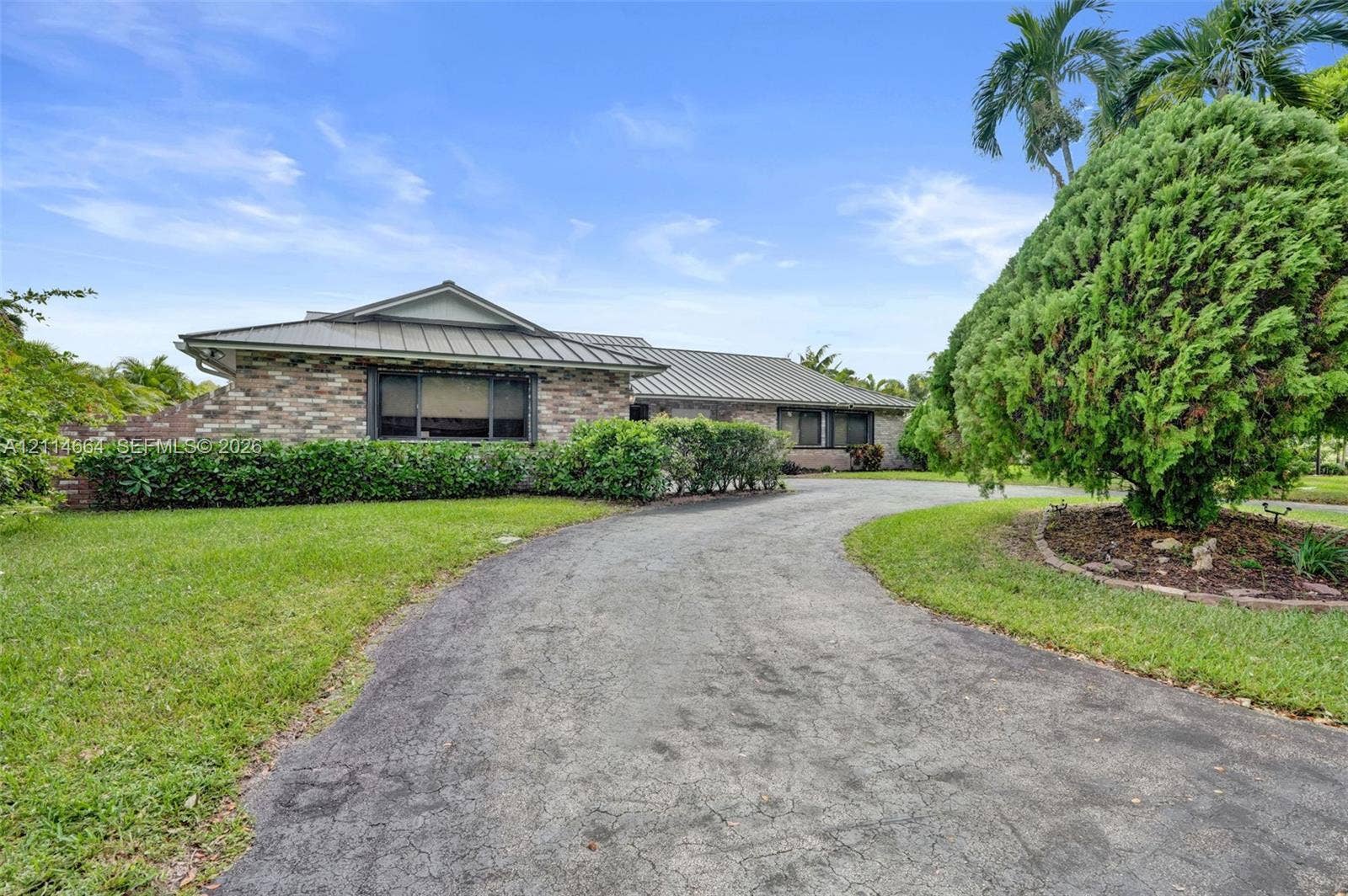 11164 NW 10th Place, Coral Springs, FL 33071 Single-story exterior featuring multi-toned masonry, a standing seam metal roof, and a paved circular driveway set amidst mature landscaping