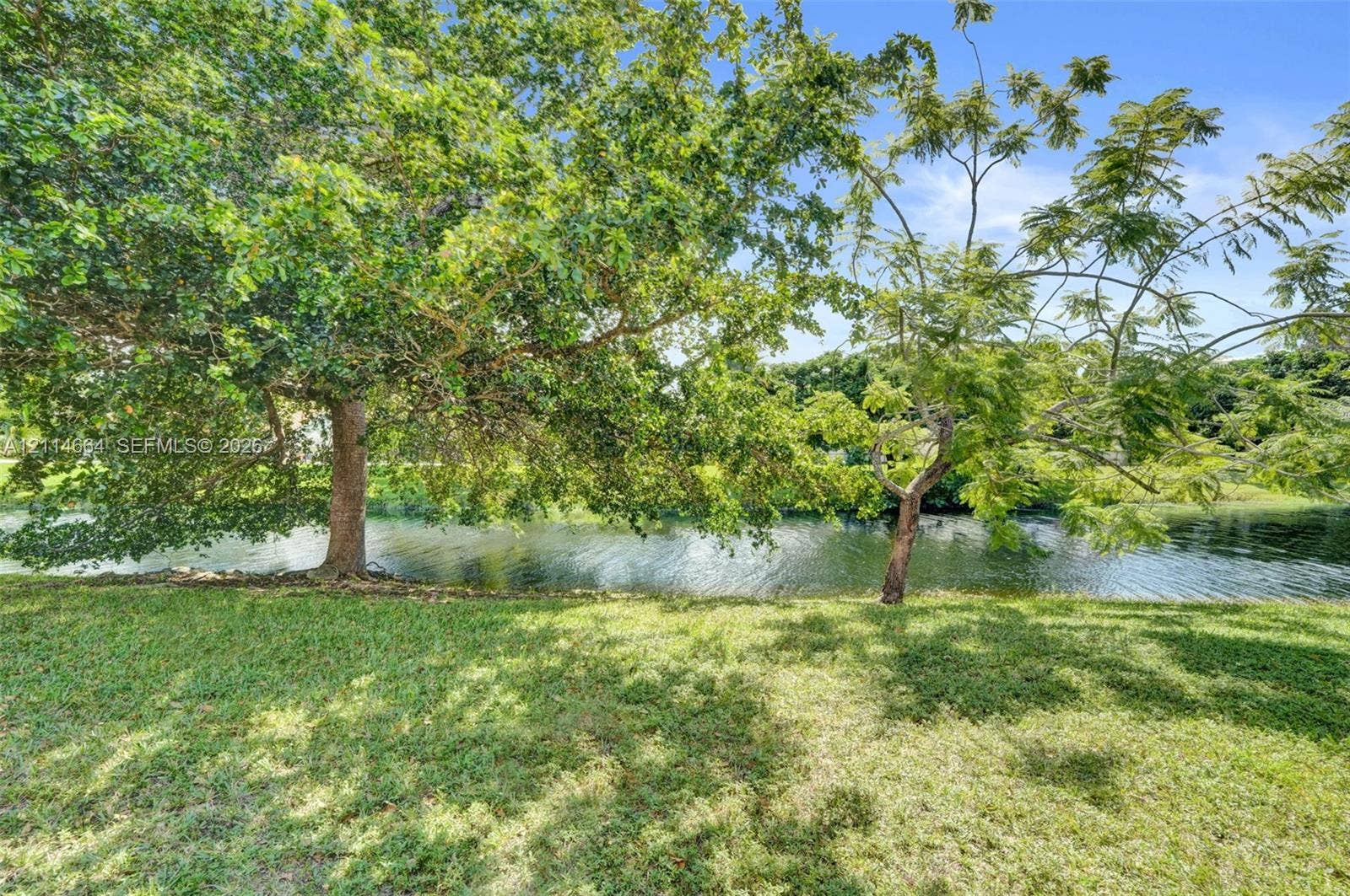 11164 NW 10th Place, Coral Springs, FL 33071 Expansive grounds featuring a water frontage, mature shade trees, and a grass lawn