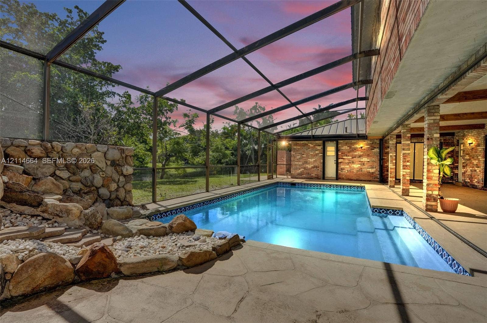 11164 NW 10th Place, Coral Springs, FL 33071 Screened-in pool area featuring a natural stone water feature, patterned stone decking, and brick exterior walls