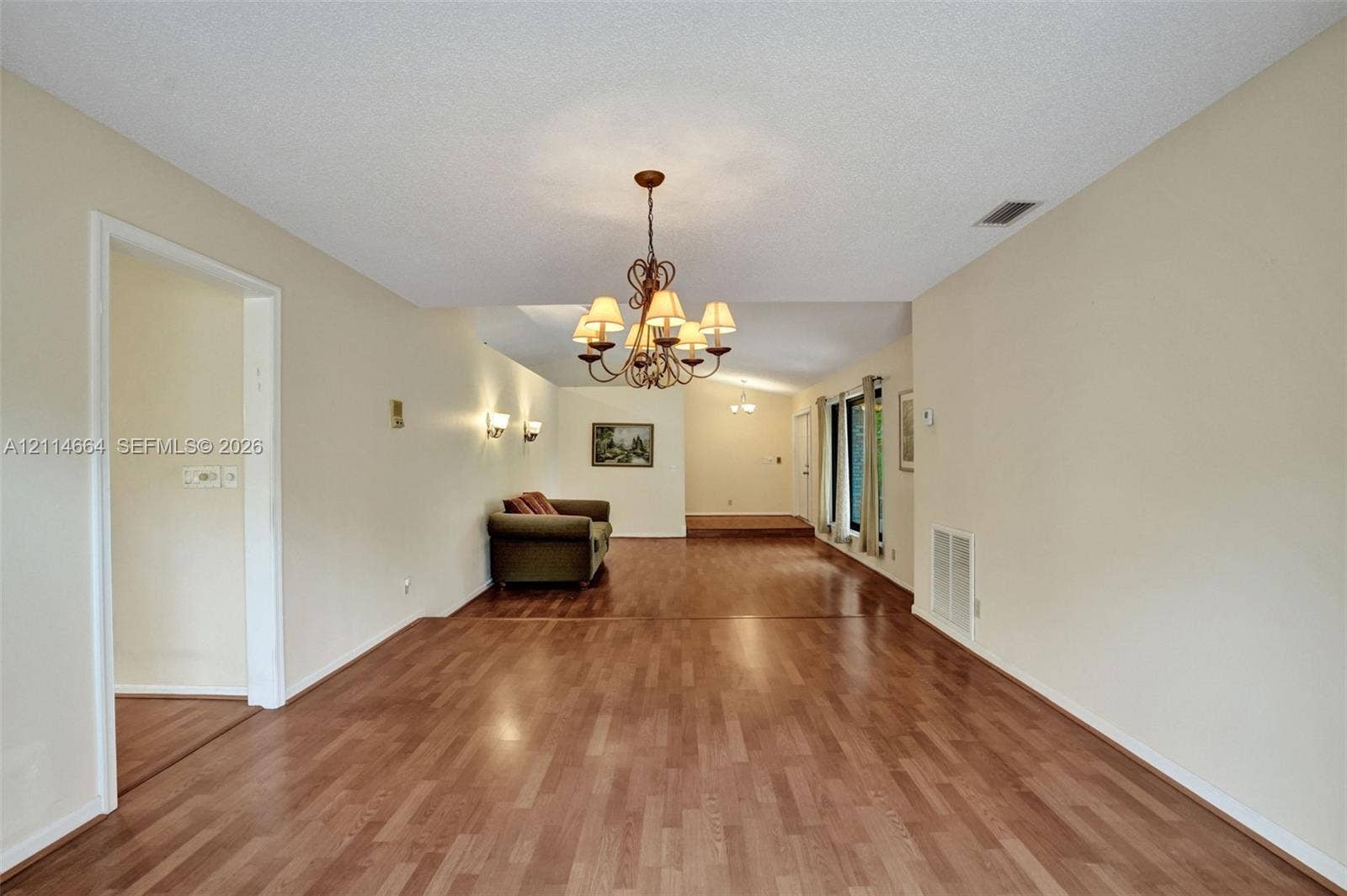 11164 NW 10th Place, Coral Springs, FL 33071 Open-concept interior featuring wood-finish flooring, vaulted ceilings, a multi-arm chandelier, and wall-mounted sconces