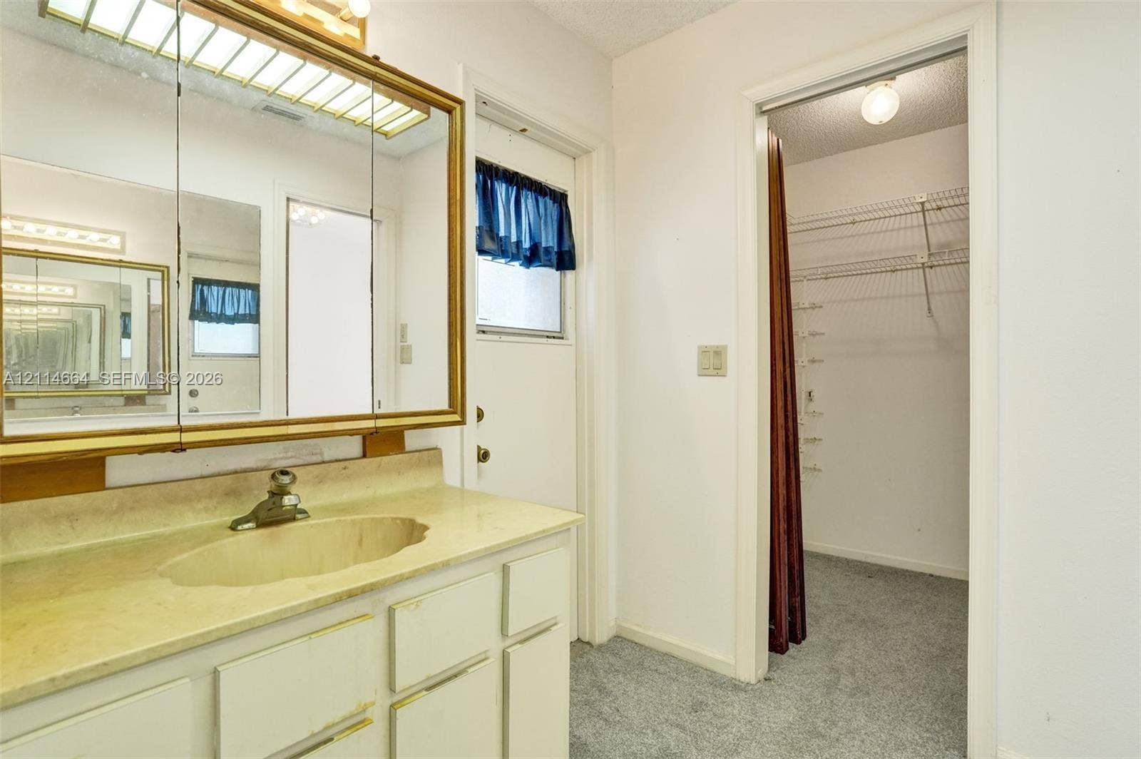 11164 NW 10th Place, Coral Springs, FL 33071 Vanity featuring an integrated sink, stone-finish countertop, brass-toned medicine cabinet, and built-in shelving within the closet