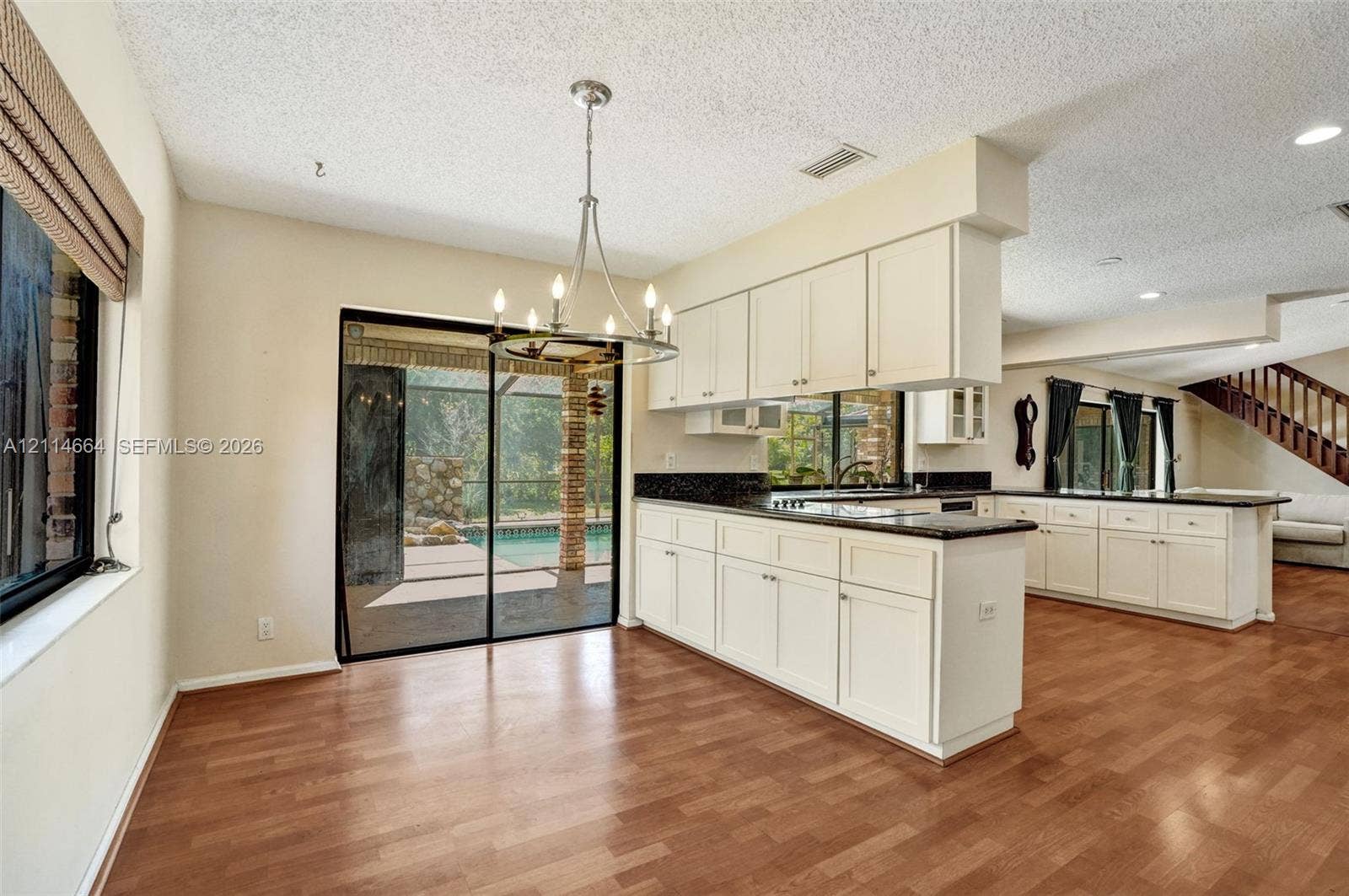 11164 NW 10th Place, Coral Springs, FL 33071 Kitchen featuring white shaker-style cabinetry, dark stone-surface countertops, wood-finish flooring, a metal multi-arm chandelier, and a sliding glass door