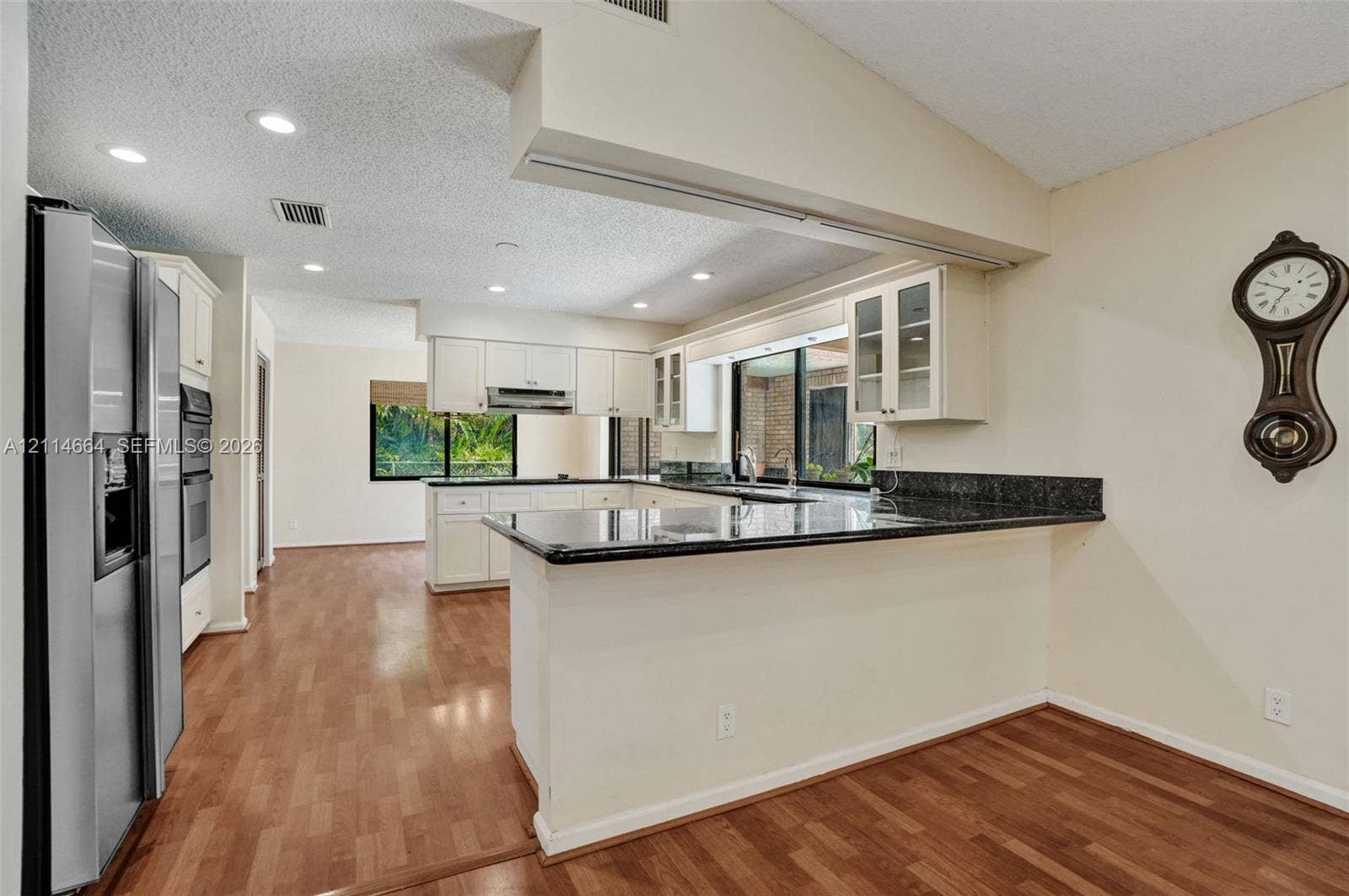 11164 NW 10th Place, Coral Springs, FL 33071 Kitchen featuring a breakfast bar, stone-surface countertops, white cabinetry with glass-panel upper doors, stainless steel wall-mounted oven, and wood-finish flooring