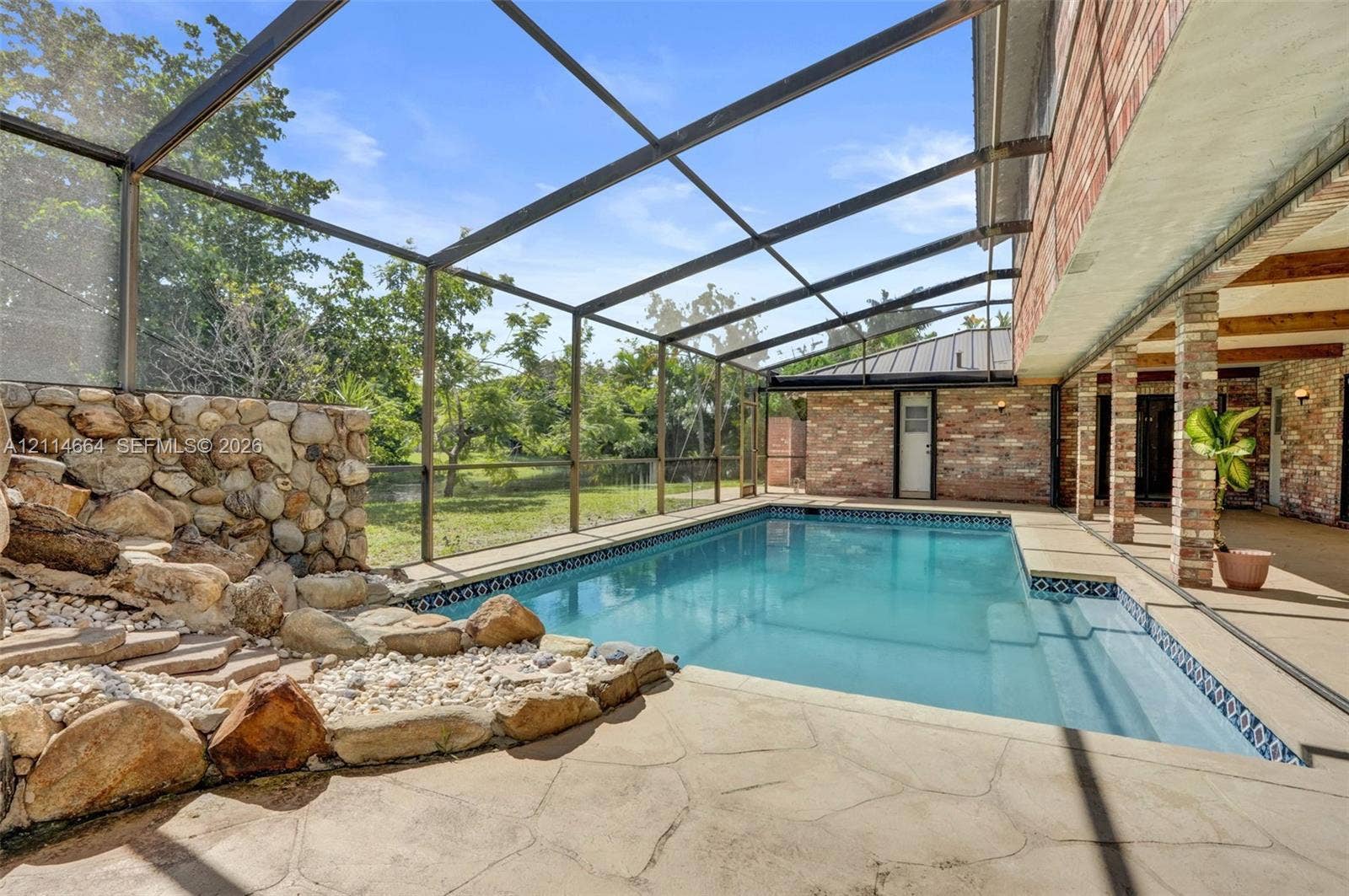 11164 NW 10th Place, Coral Springs, FL 33071 Screen-enclosed pool area featuring a natural stone water feature, patterned concrete decking, covered patio space, and brick architectural detailing