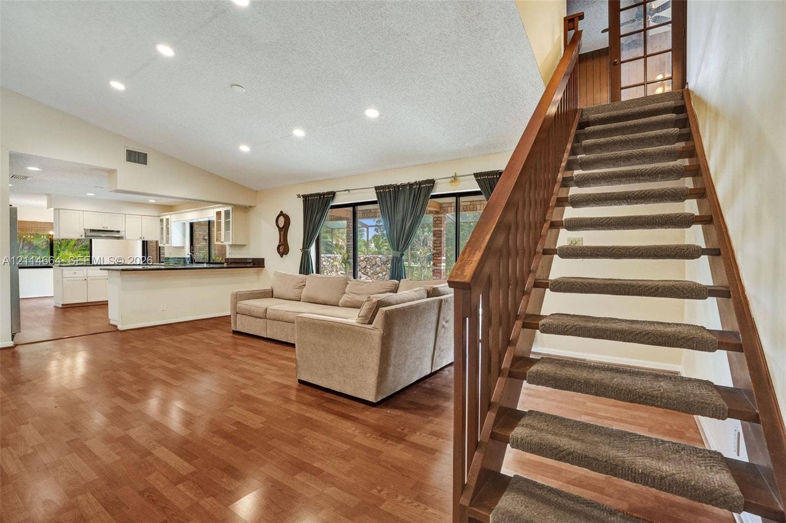 11164 NW 10th Place, Coral Springs, FL 33071 Open-concept living space featuring wood-finish flooring, vaulted ceilings with recessed lighting, a wooden staircase with carpeted treads, and sliding glass doors
