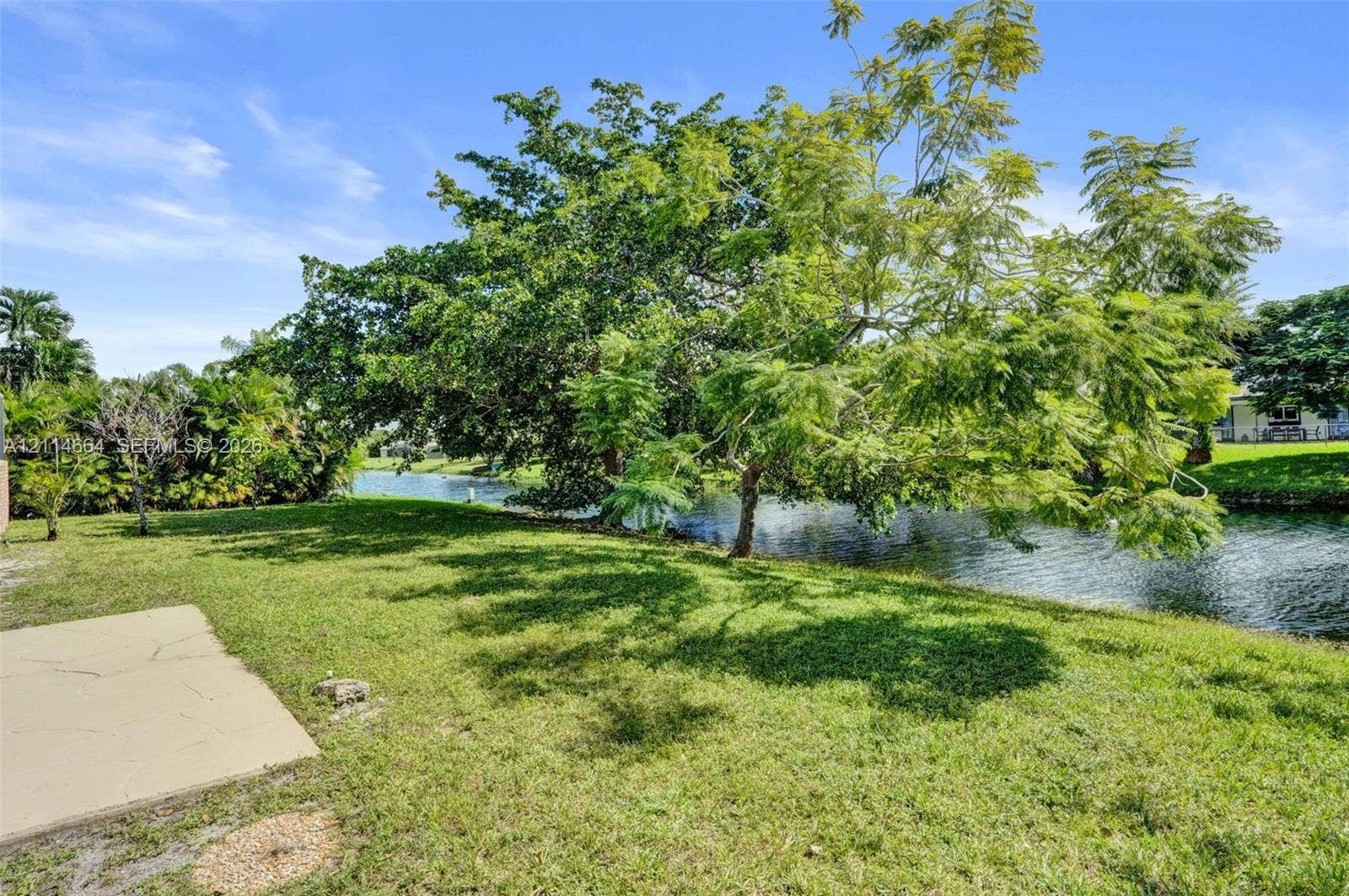 11164 NW 10th Place, Coral Springs, FL 33071 Rear grounds featuring a waterfront lot, concrete hardscaping, manicured lawn, and mature trees