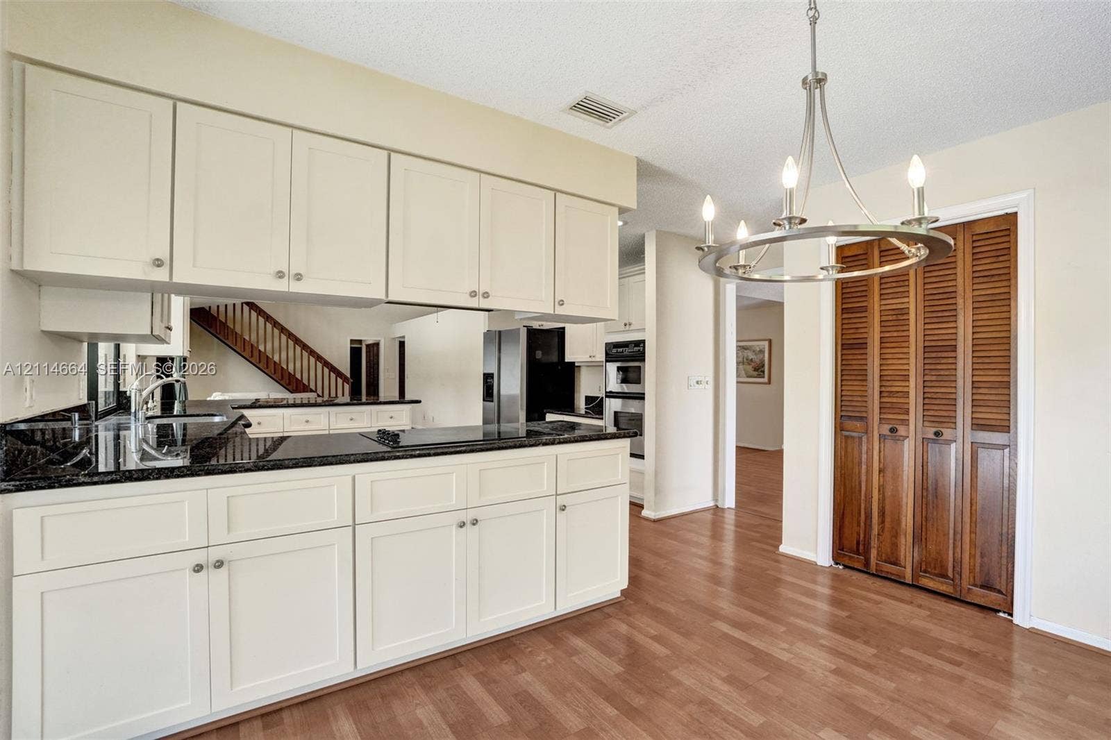 11164 NW 10th Place, Coral Springs, FL 33071 Kitchen featuring white shaker-style cabinetry, dark stone-finish countertops, stainless steel wall-mounted oven, wood-finish flooring, and a circular metal chandelier