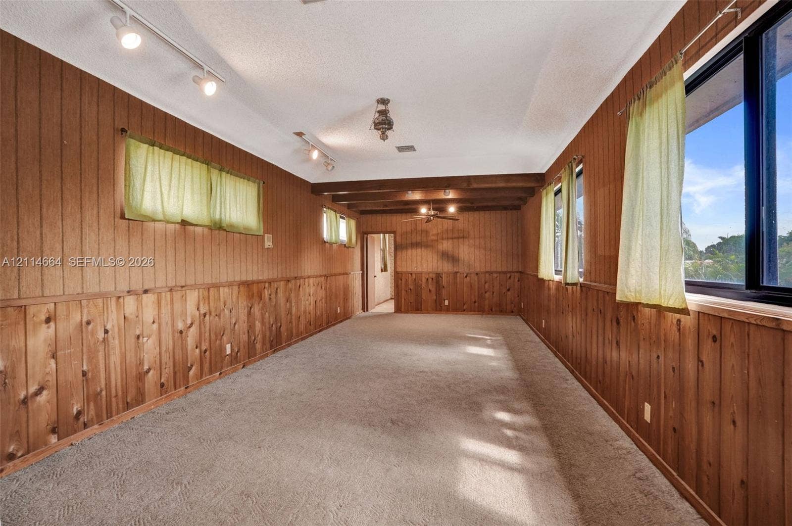 11164 NW 10th Place, Coral Springs, FL 33071 Interior space featuring wood-paneled walls, exposed ceiling beams, adjustable track lighting, and wall-to-wall carpeting
