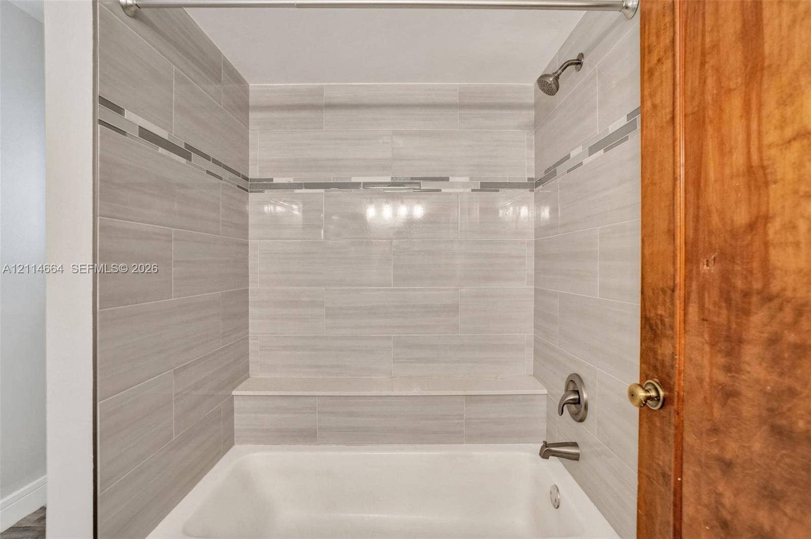 11164 NW 10th Place, Coral Springs, FL 33071 Bathtub enclosure featuring neutral-toned ceramic tile surround, decorative glass tile inlay, built-in shelving ledge, and wall-mounted metal fixtures
