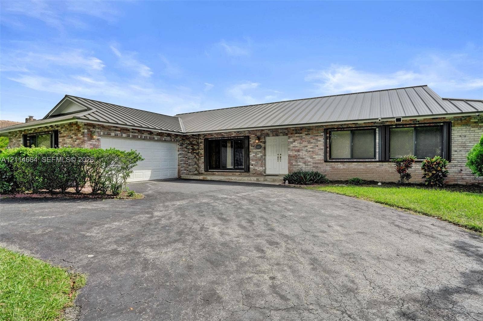 11164 NW 10th Place, Coral Springs, FL 33071 Single-story brick exterior featuring a multi-paneled metal roof, double-entry front doors, and an attached two-car garage
