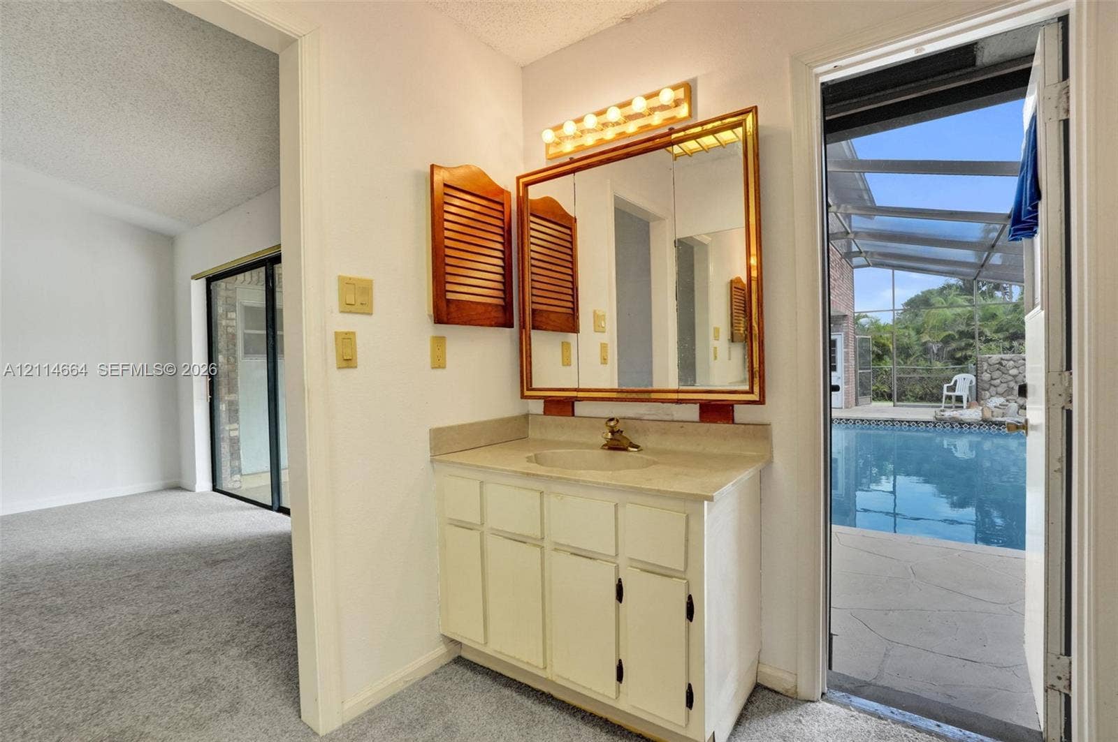 11164 NW 10th Place, Coral Springs, FL 33071 Vanity with stone-finish countertop, integrated sink, large rectangular mirror, multi-bulb overhead lighting, and dual louvered-style wall cabinets