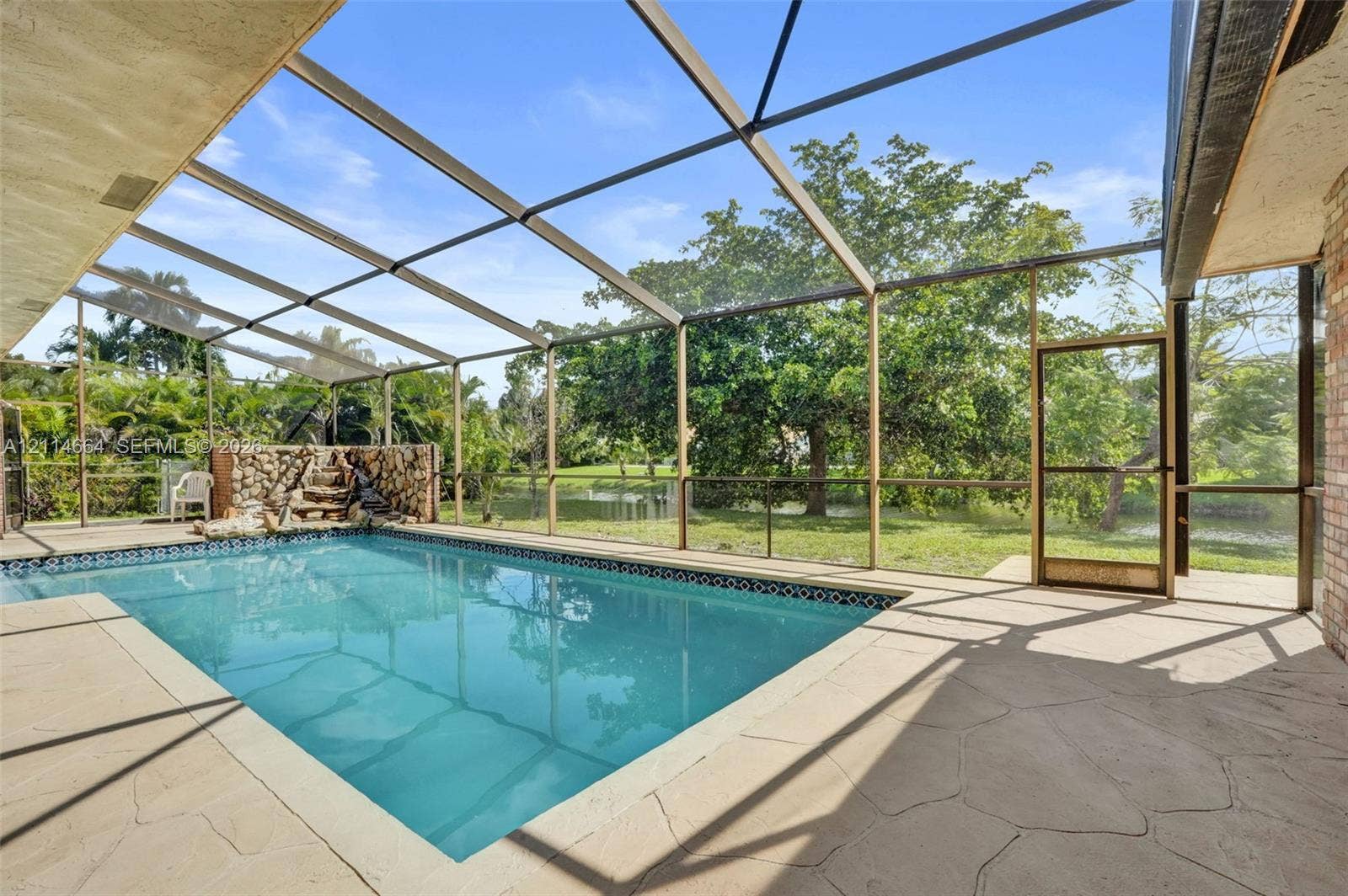 11164 NW 10th Place, Coral Springs, FL 33071 Screen-enclosed swimming pool featuring a flagstone-style patio, built-in stone waterfall feature, and direct water frontage