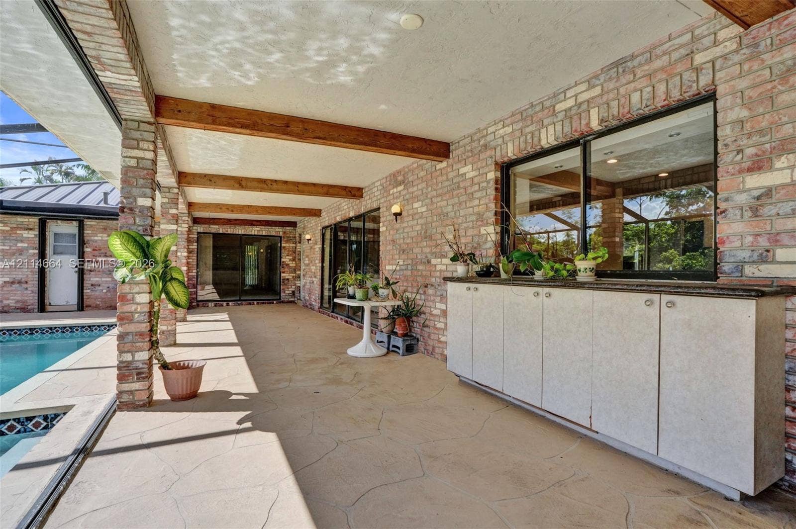 11164 NW 10th Place, Coral Springs, FL 33071 Covered outdoor patio featuring exposed wood beams, brick masonry walls, stamped concrete flooring, and built-in cabinetry with a stone countertop