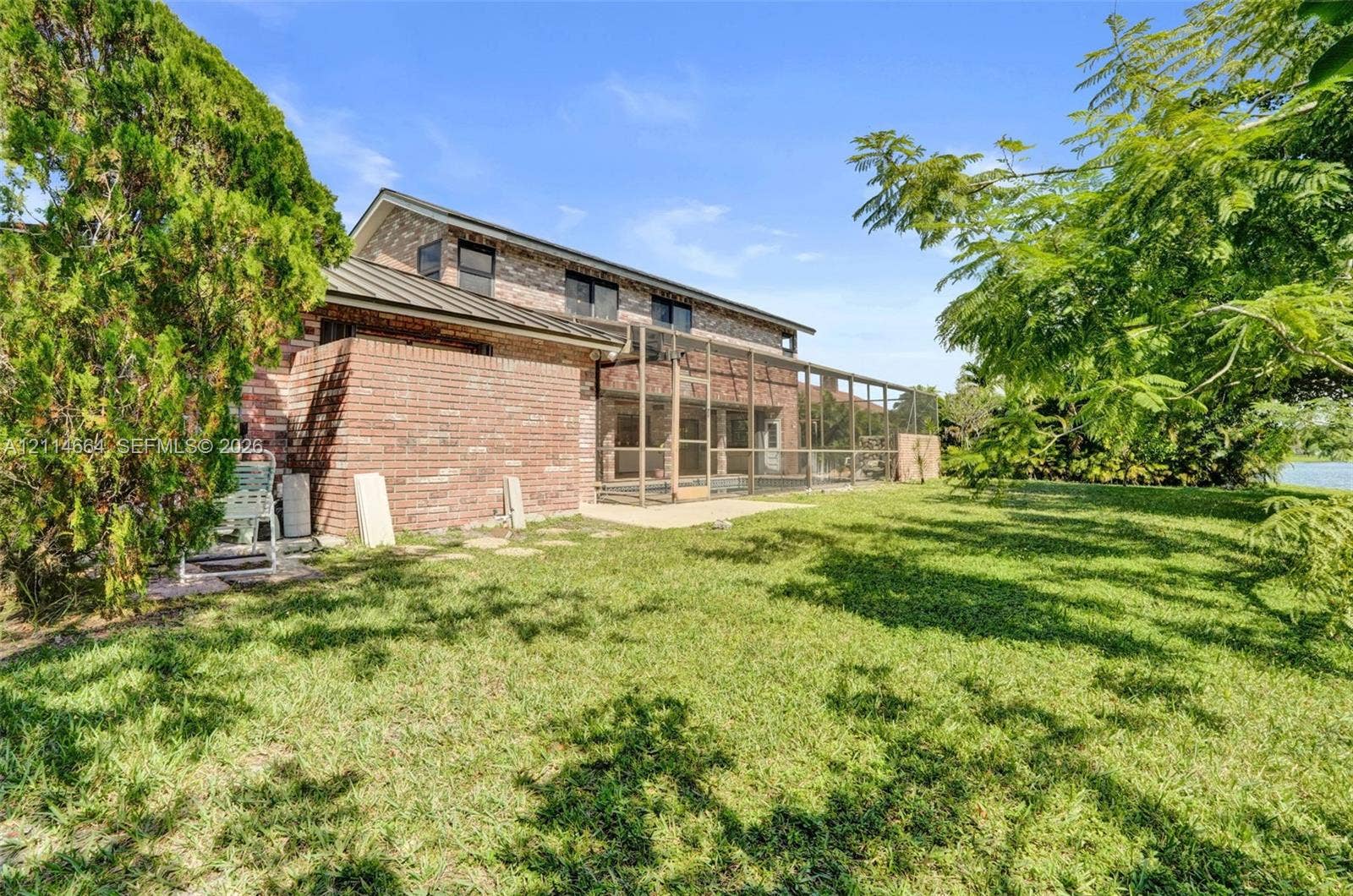 11164 NW 10th Place, Coral Springs, FL 33071 Brick exterior residence featuring a metal roof, screened-in porch, and expansive grassy yard