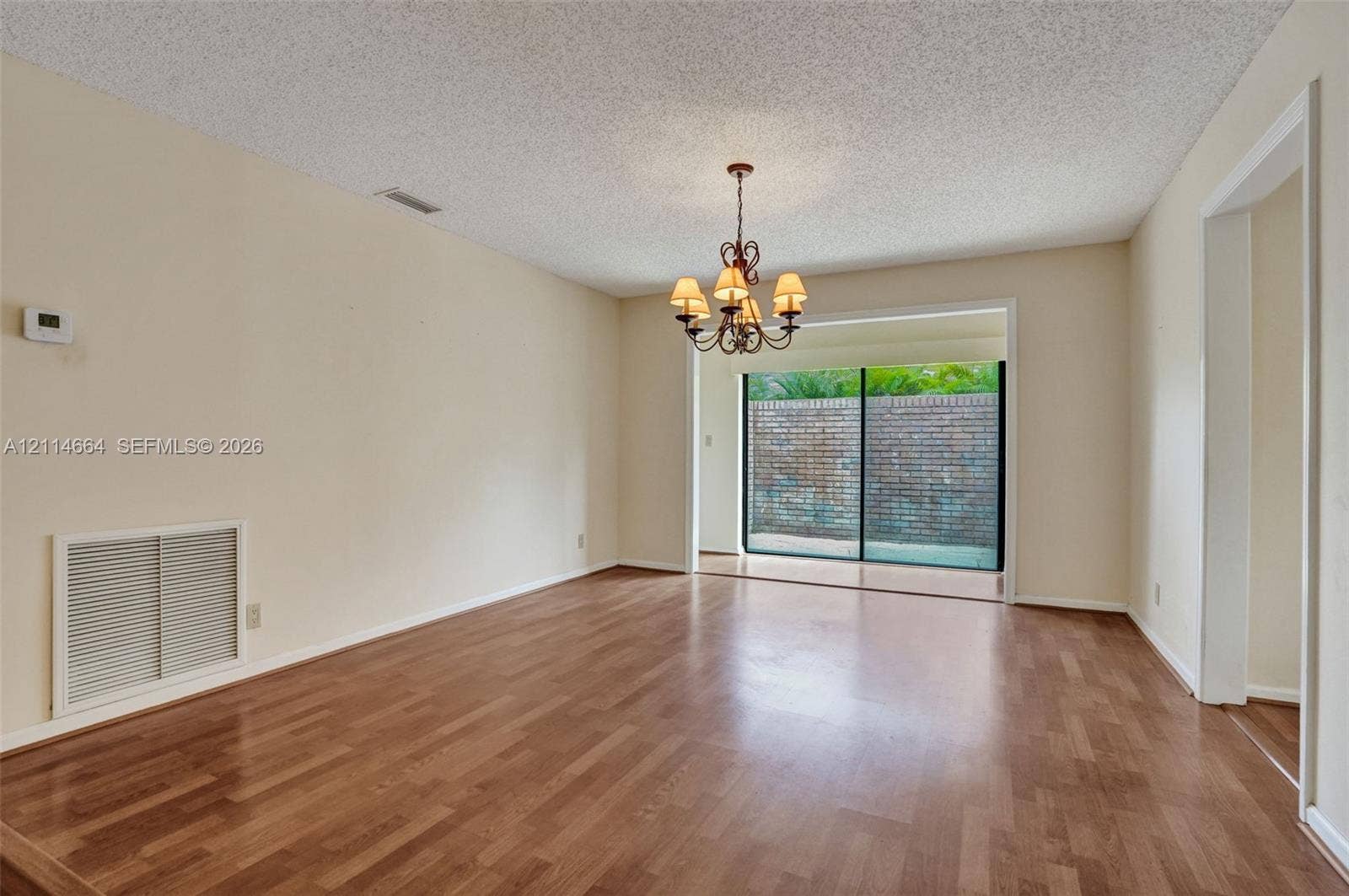 11164 NW 10th Place, Coral Springs, FL 33071 Living area featuring wood-finish flooring, a multi-arm chandelier, and sliding glass doors with exterior brick wall visibility