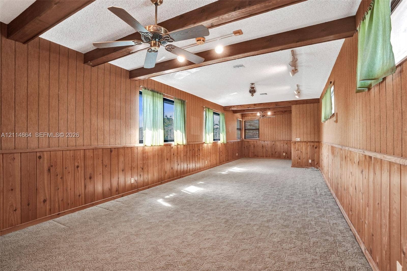 11164 NW 10th Place, Coral Springs, FL 33071 Interior space featuring wood paneling, exposed ceiling beams, carpeted flooring, a ceiling fan, and adjustable track lighting