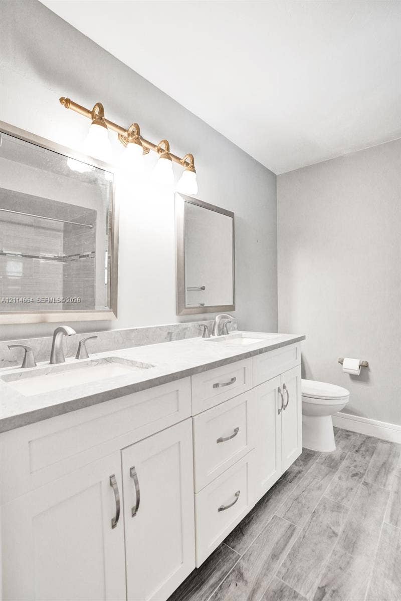 11164 NW 10th Place, Coral Springs, FL 33071 Dual-sink vanity with stone countertop, white shaker-style cabinetry, metallic hardware, and wood-finish flooring