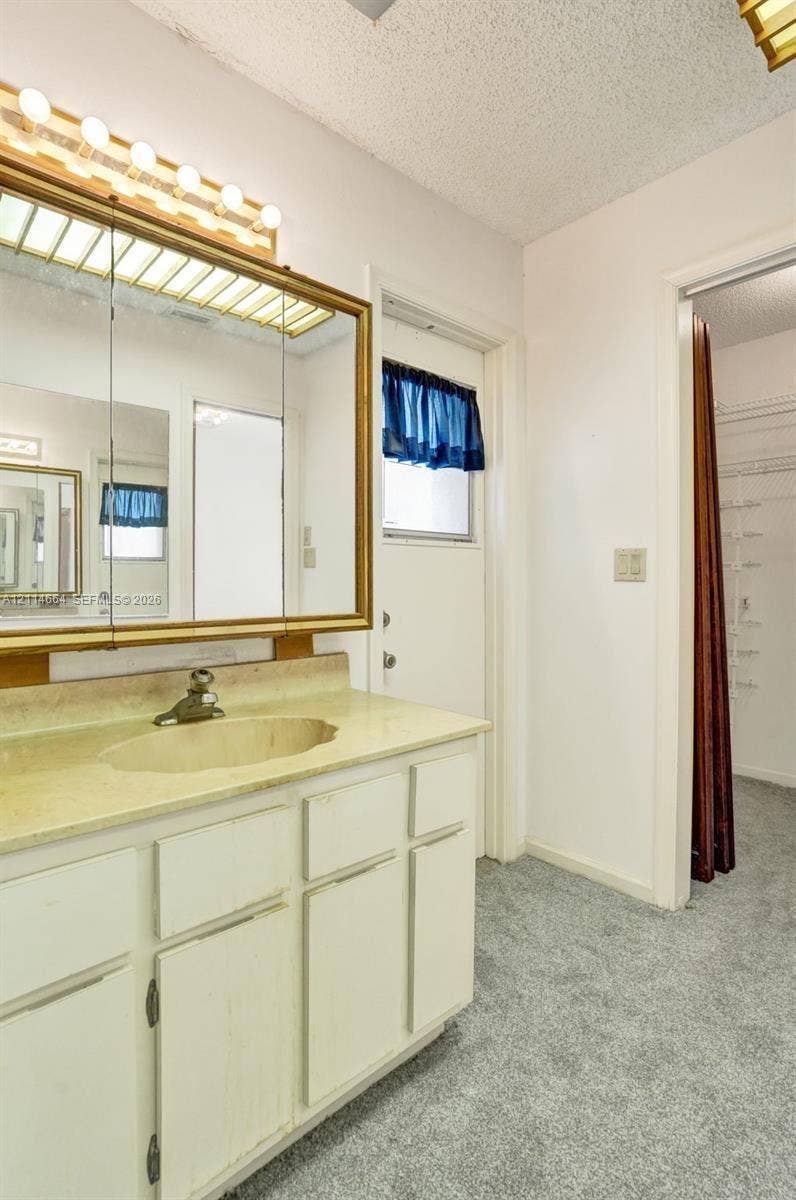 11164 NW 10th Place, Coral Springs, FL 33071 Bathroom featuring white cabinetry, an integrated sink with a stone-finish countertop, a large framed medicine cabinet, and overhead theater-style lighting
