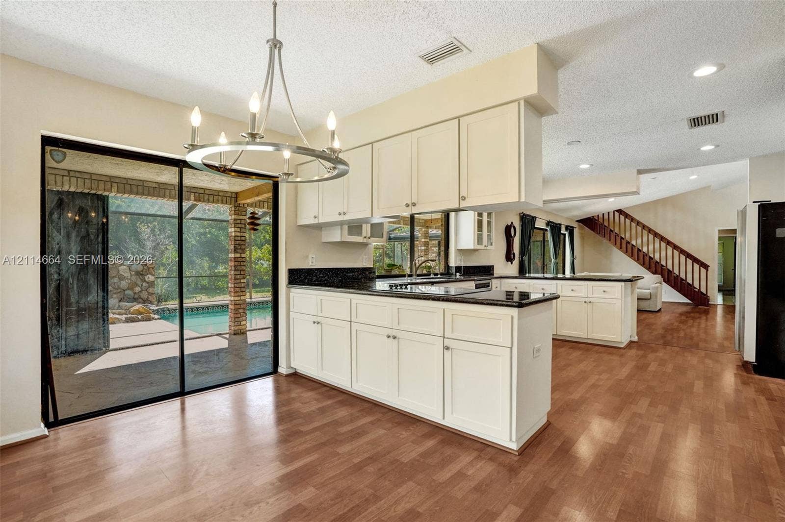 11164 NW 10th Place, Coral Springs, FL 33071 Kitchen featuring white cabinetry, dark stone countertops, recessed lighting, a chandelier, and wood-finish flooring with sliding glass door access to an outdoor pool area