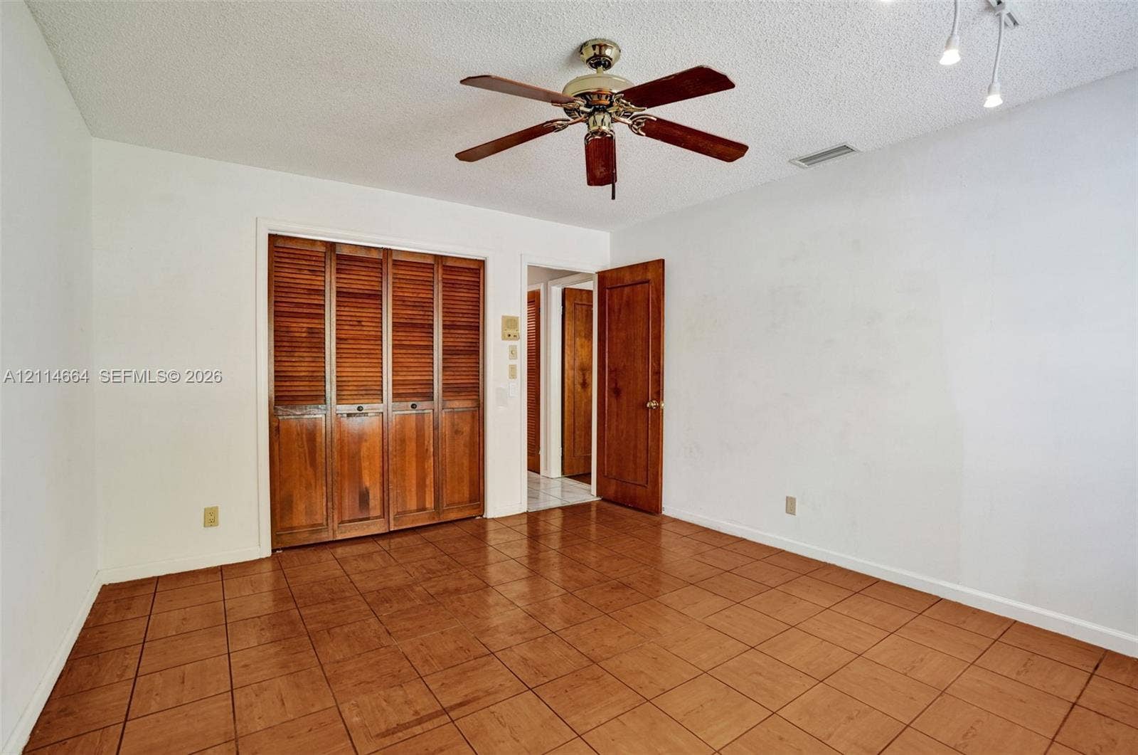 11164 NW 10th Place, Coral Springs, FL 33071 Room featuring ceramic tile flooring, built-in wooden louvered closet doors, a matching wooden interior door, and a ceiling-mounted fan with light fixture