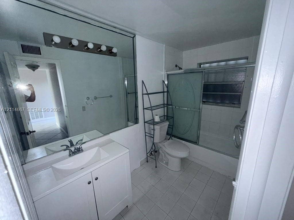 Bathroom featuring a vanity with a white basin, a full-width wall mirror, a five-light fixture, and a tub-shower combination with sliding glass doors